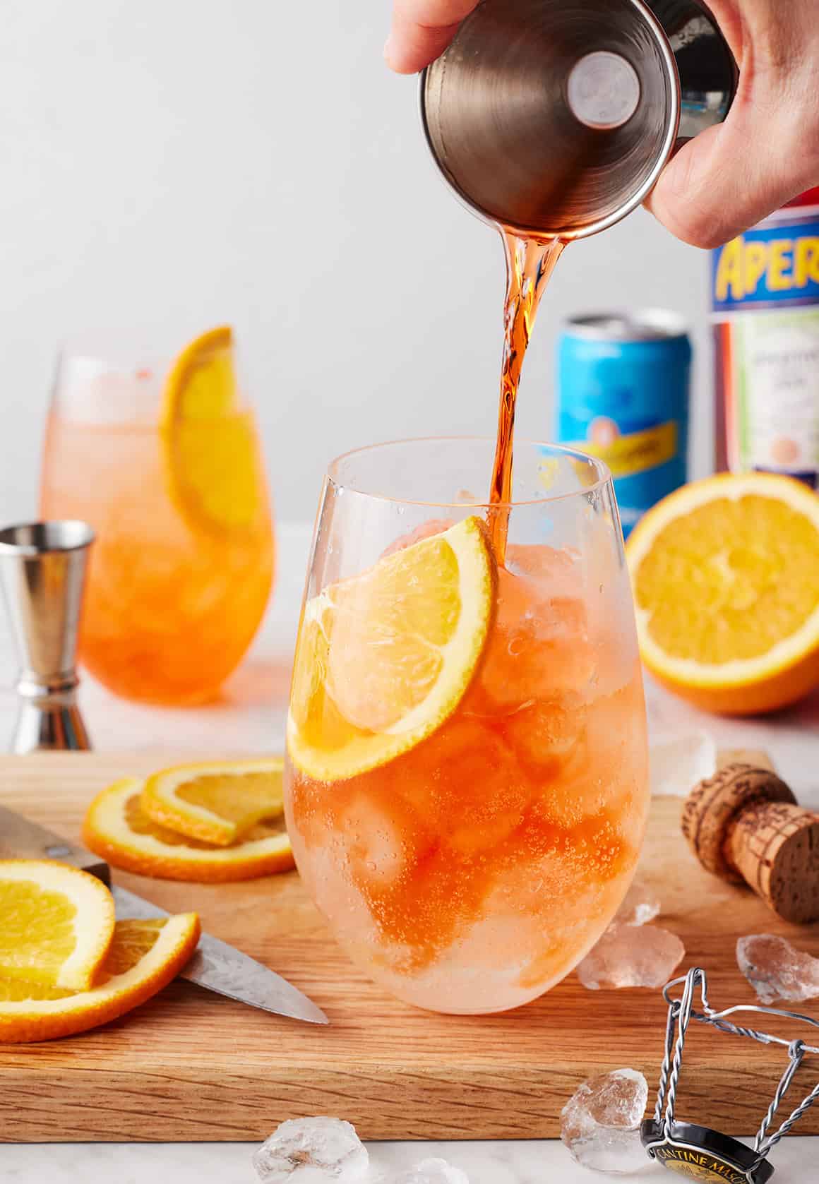 Pouring aperitif into cocktail garnished with orange slice