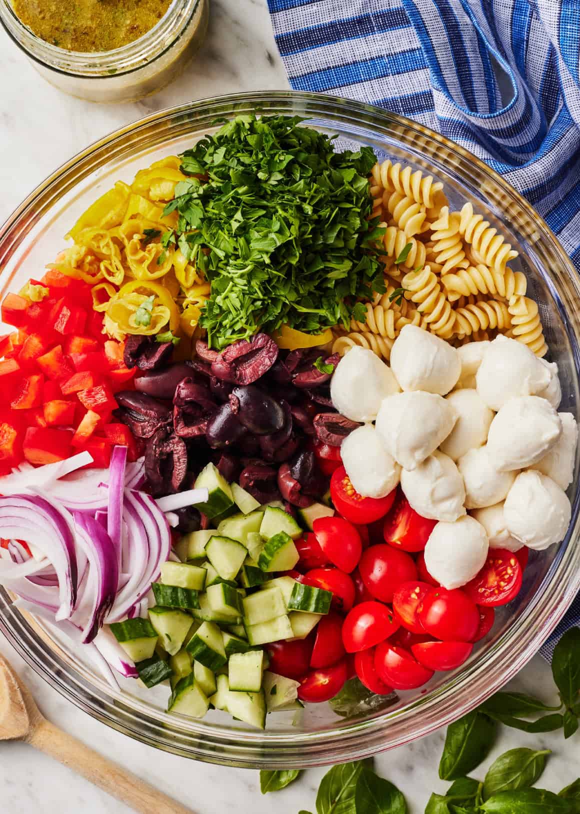 Tomatoes, cucumber, mozzarella, olives, red onion, red peppers, pepperoncini, parsley, and rotini in mixing bowl