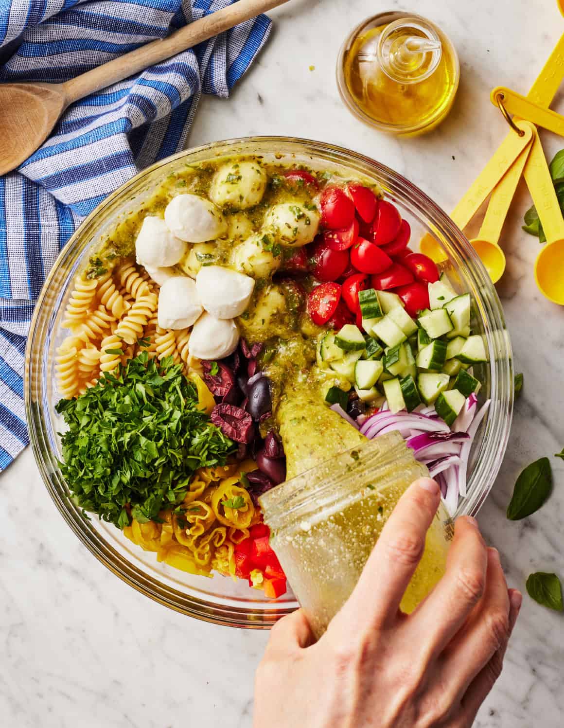 Pouring Italian dressing over pasta salad