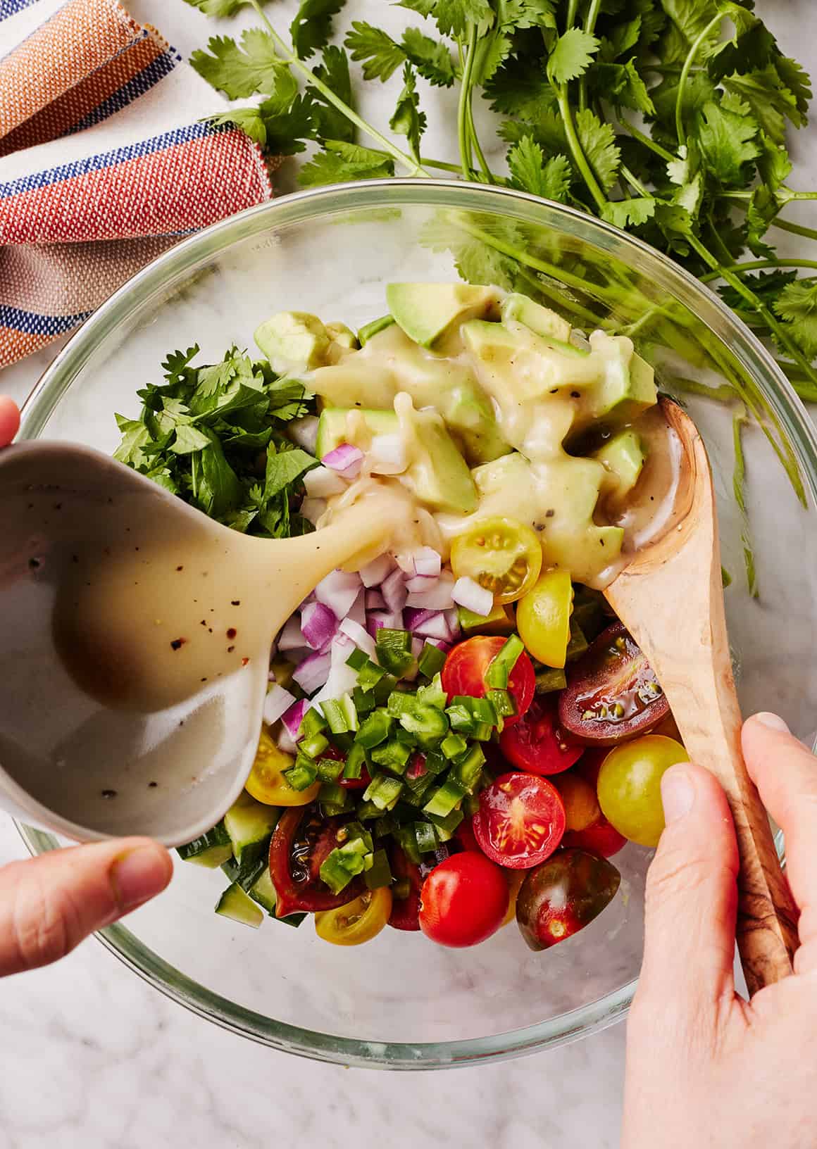 Pouring dressing over tomatoes, cucumbers, and onion in mixing bowl