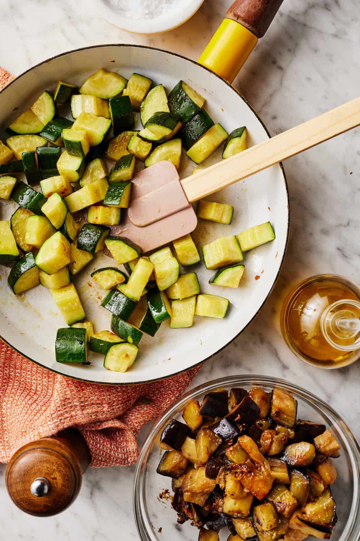 Sautéing zucchini in skillet with bowl of eggplant nearby