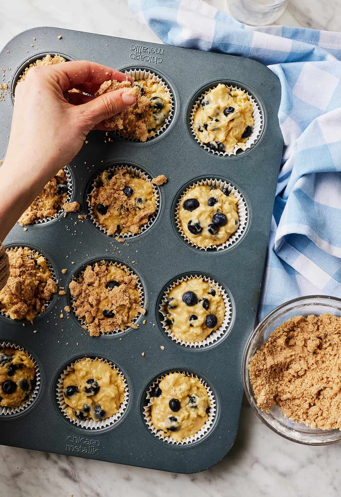 Sprinkling streusel topping over blueberry muffins in muffin pan
