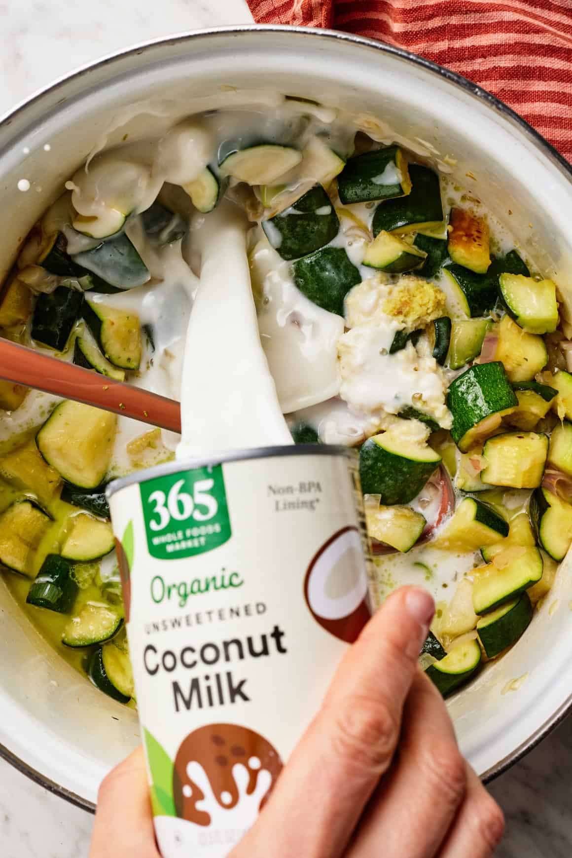 Pouring coconut milk into pot with sautéed zucchini