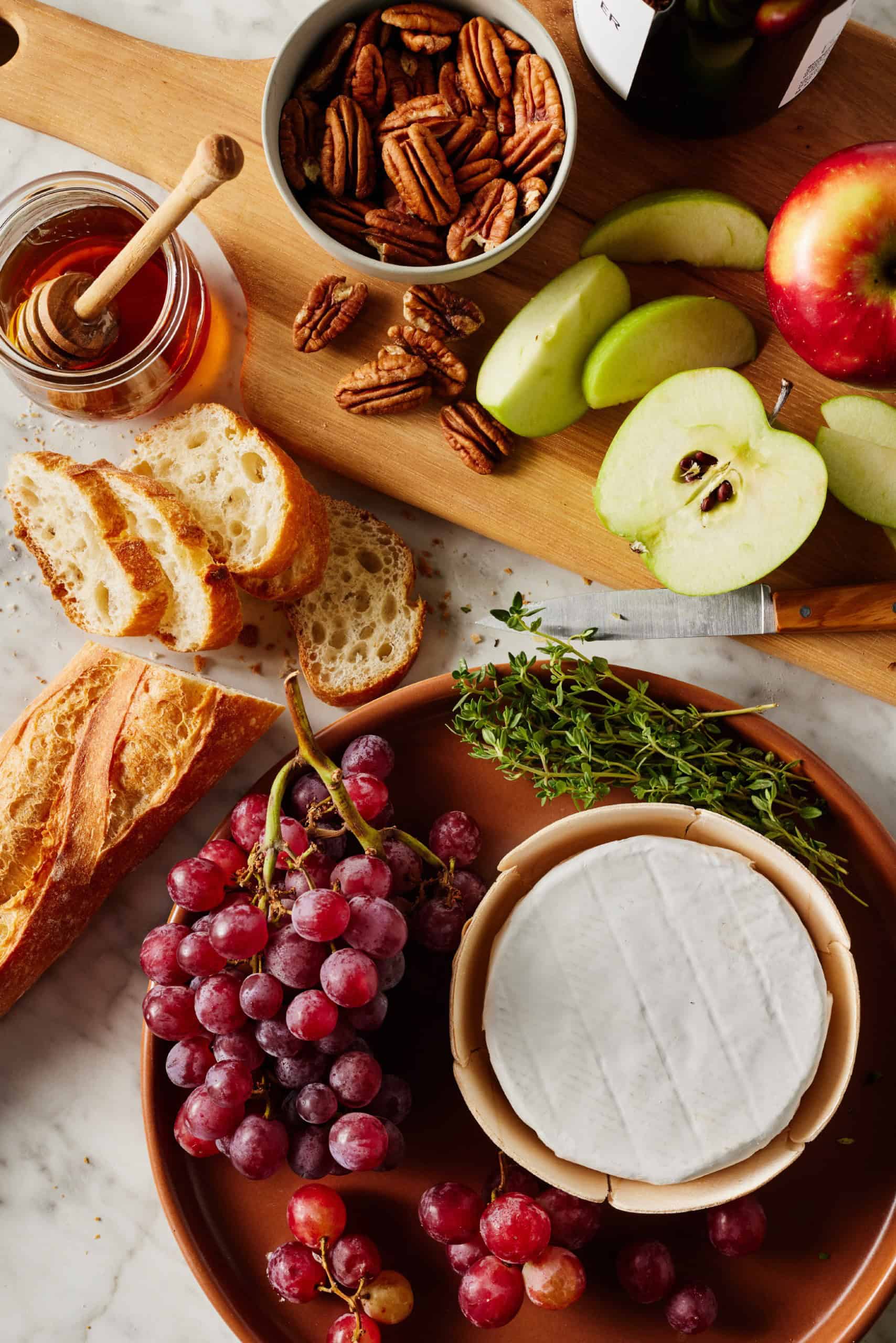 Recipe components - wheel of cheese, baguette, grapes, apples, honey, thyme, and pecans