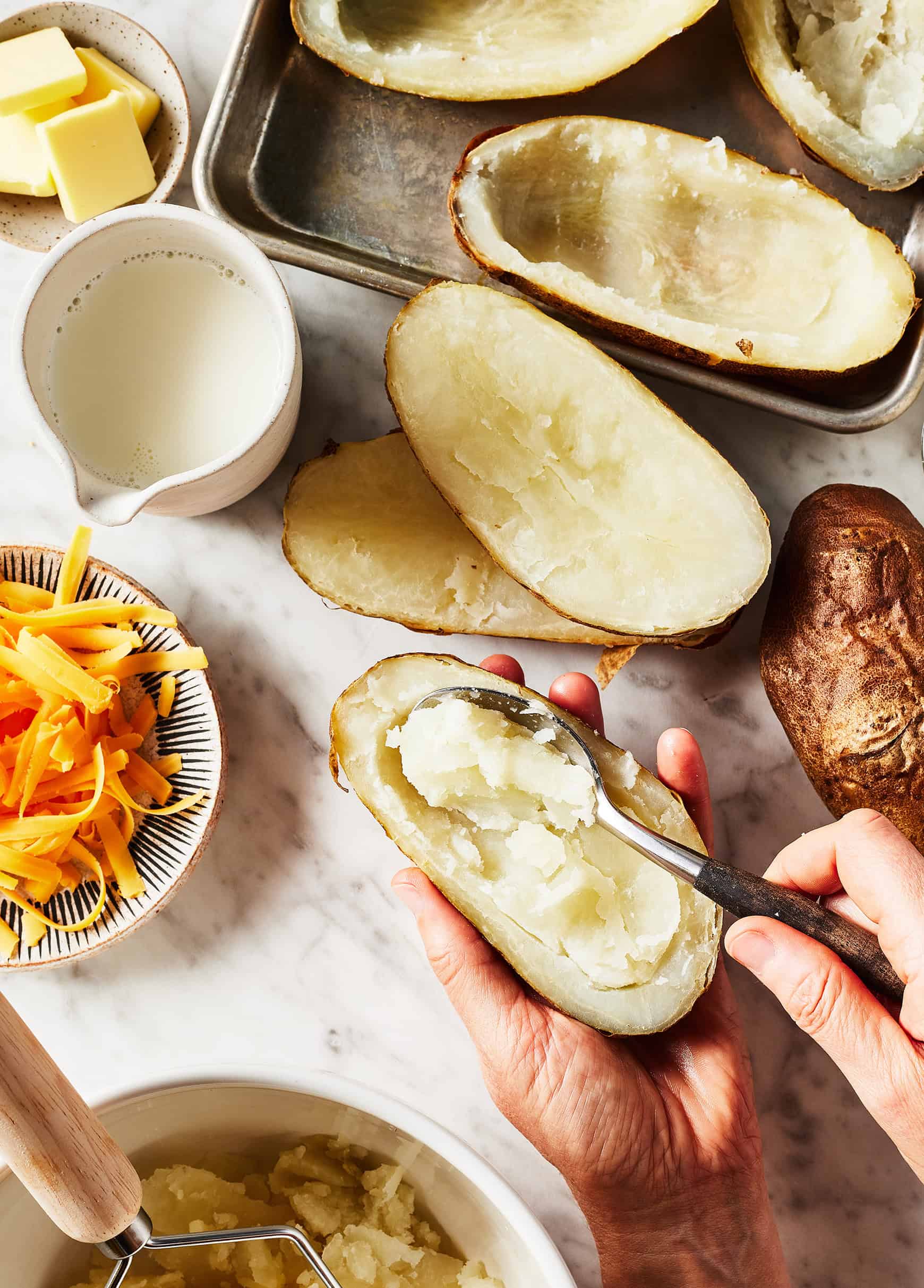 Scooping flesh out of halved baked potatoes