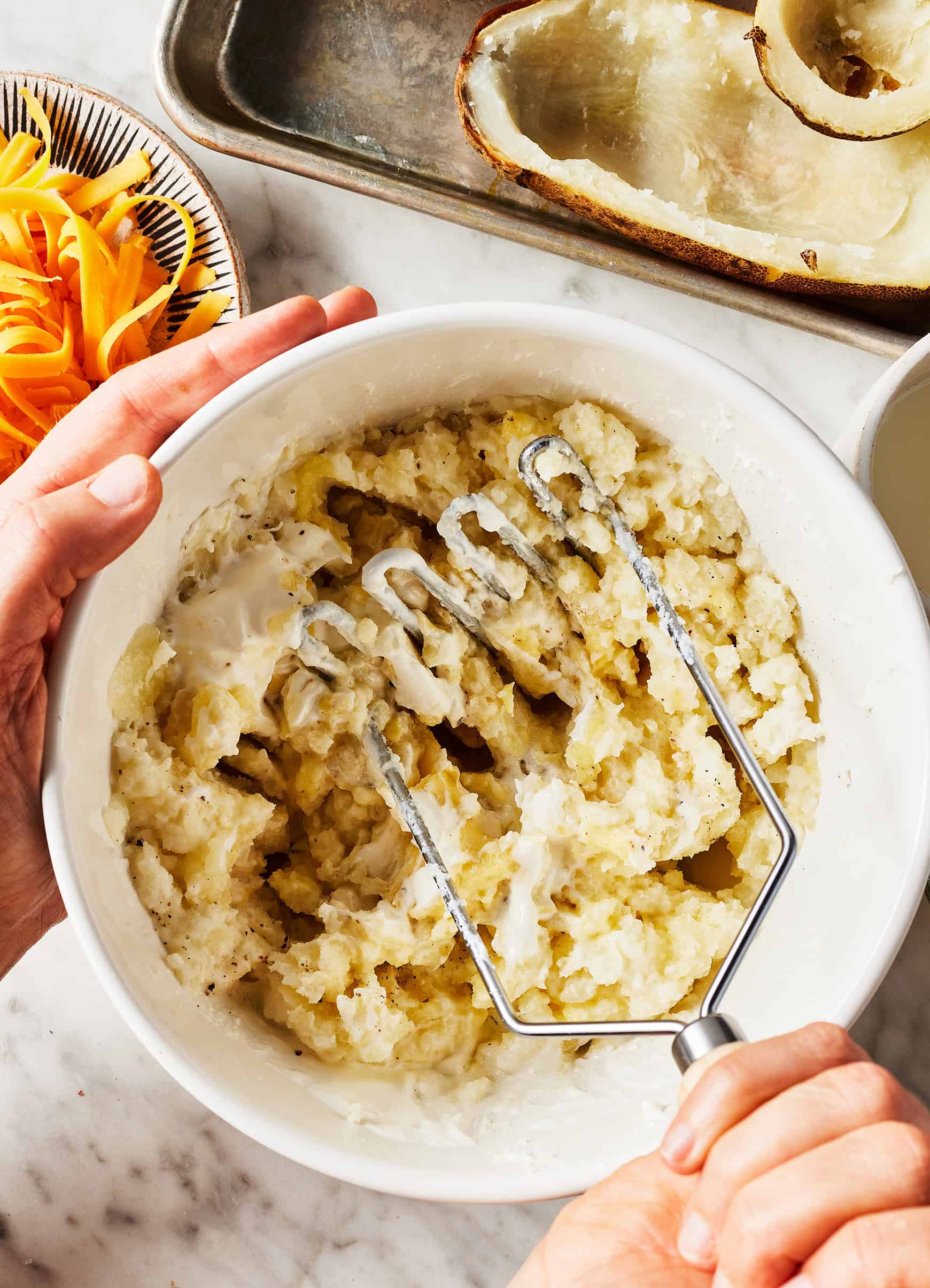 Mashing potatoes with sour cream, milk, butter, garlic, salt, and pepper