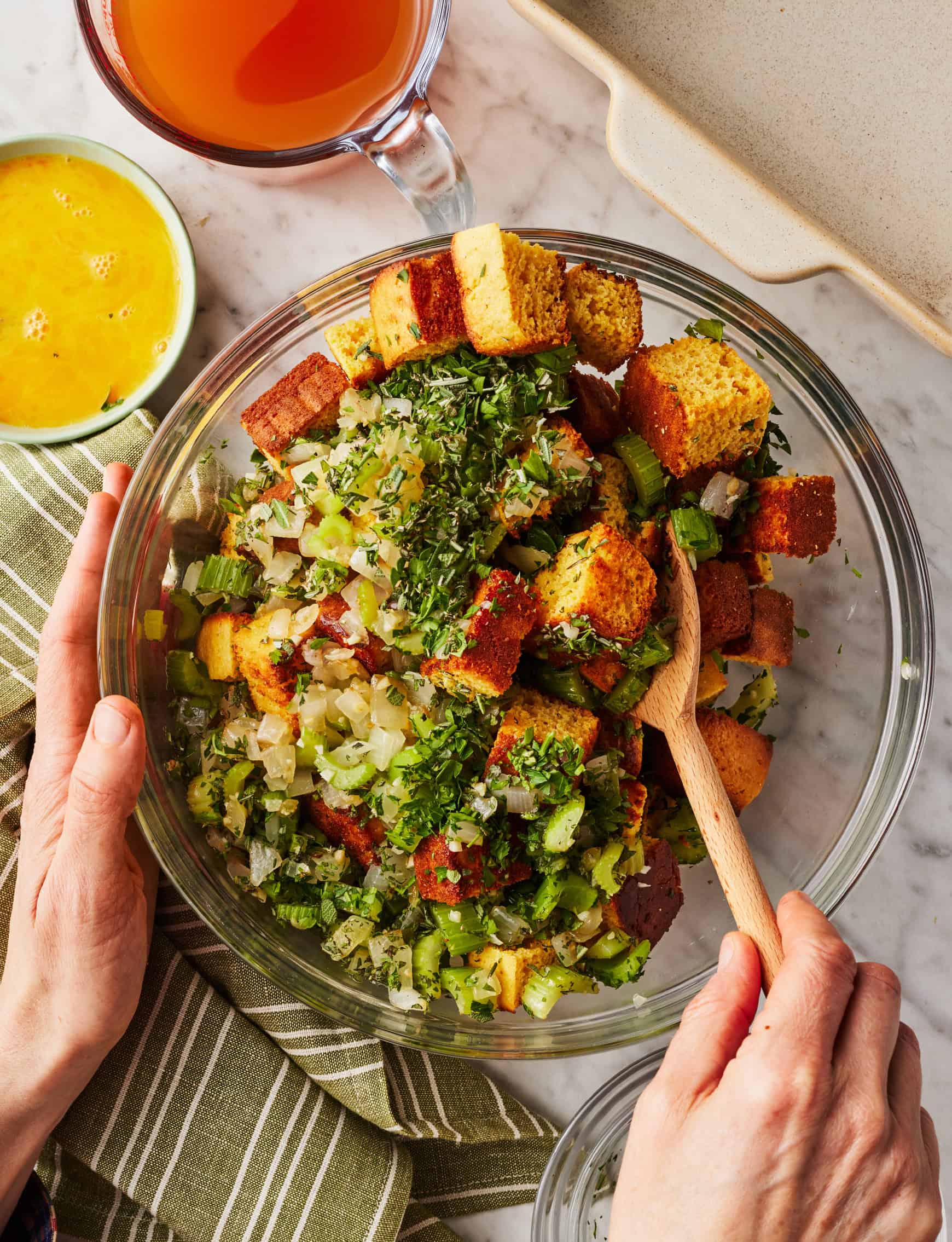 Mixing cornbread with herbs and aromatics in glass bowl