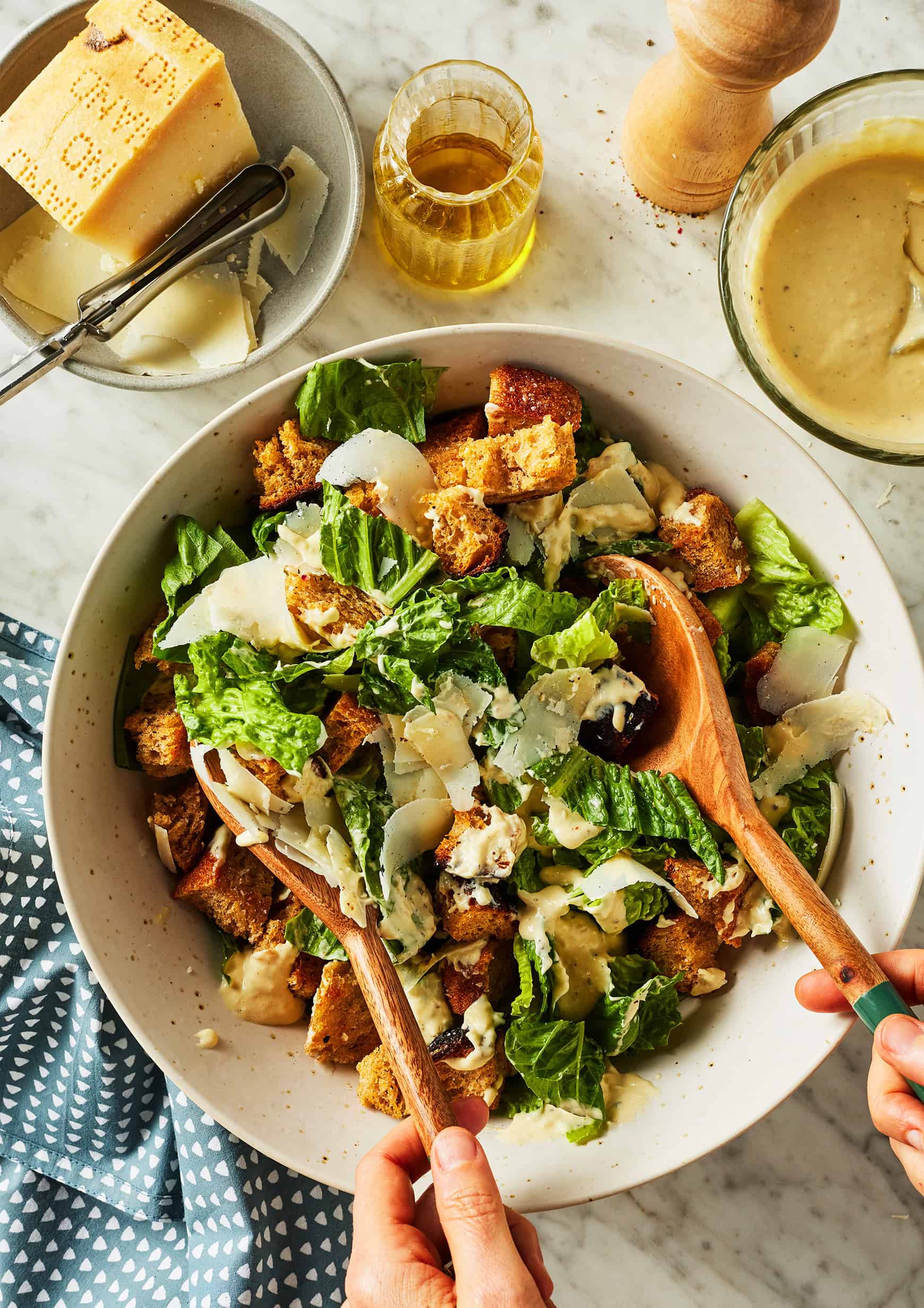 Tossing romaine lettuce with croutons, dressing, and shaved Parmesan cheese