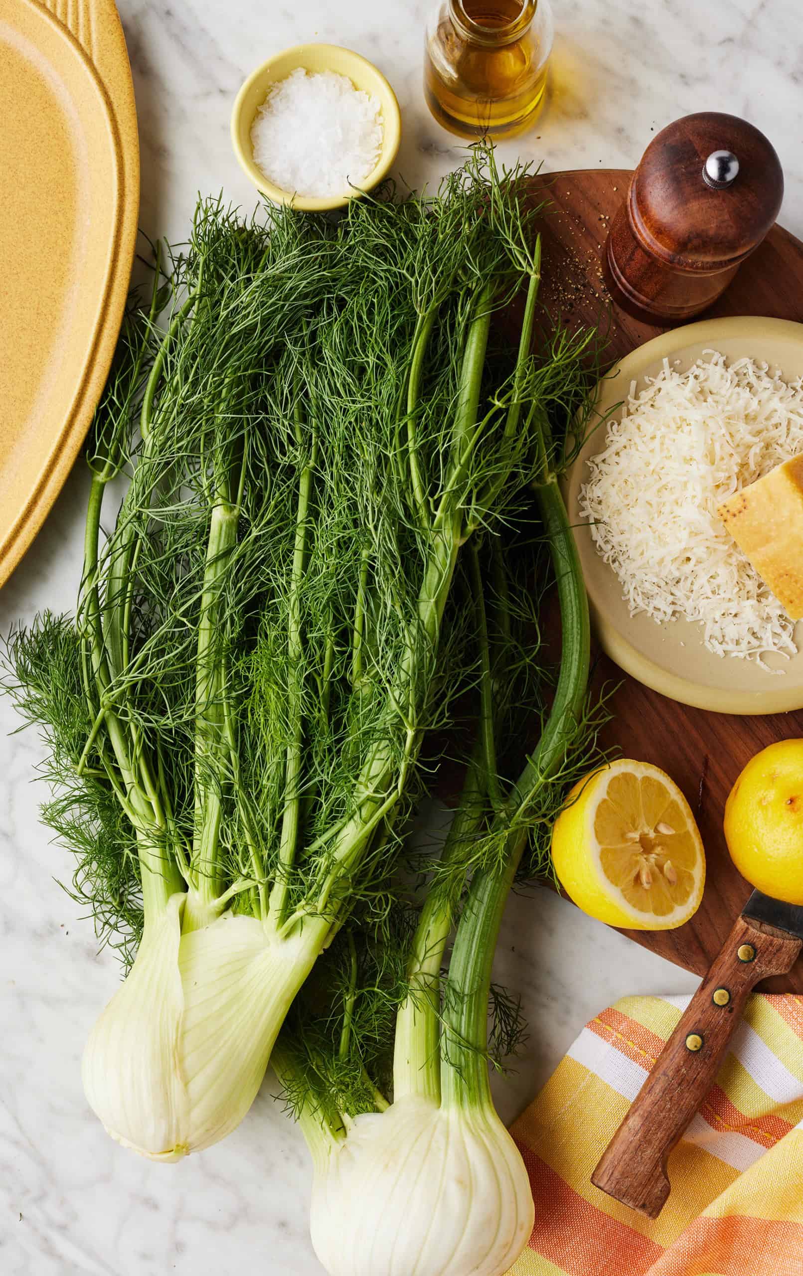 Fennel bulbs, fresh lemon, olive oil, salt, pepper, and Parmesan cheese on marble surface