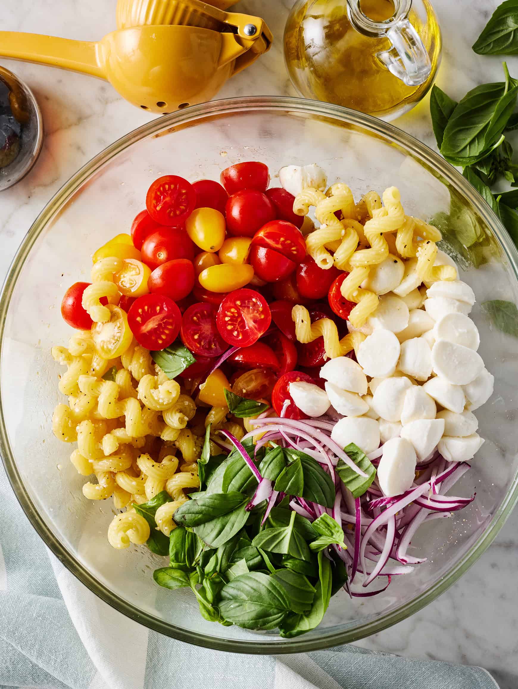 Pasta, cherry tomatoes, basil, fresh mozzarella, and red onion in a bowl
