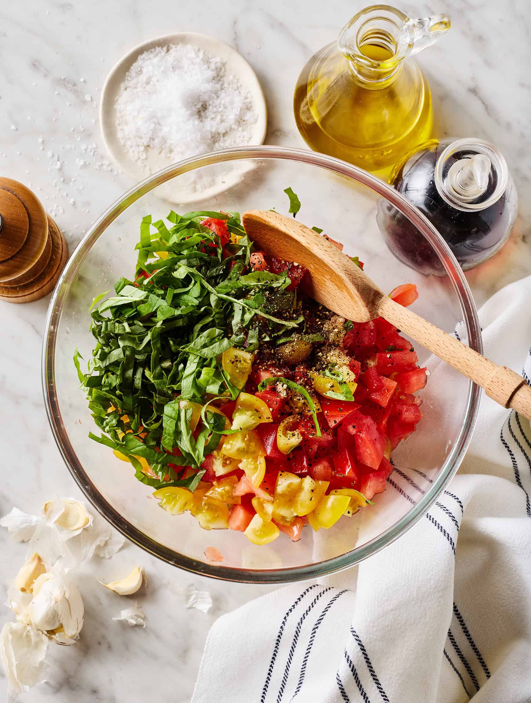 Tomatoes, basil, salt, and pepper in glass bowl with wooden spoon