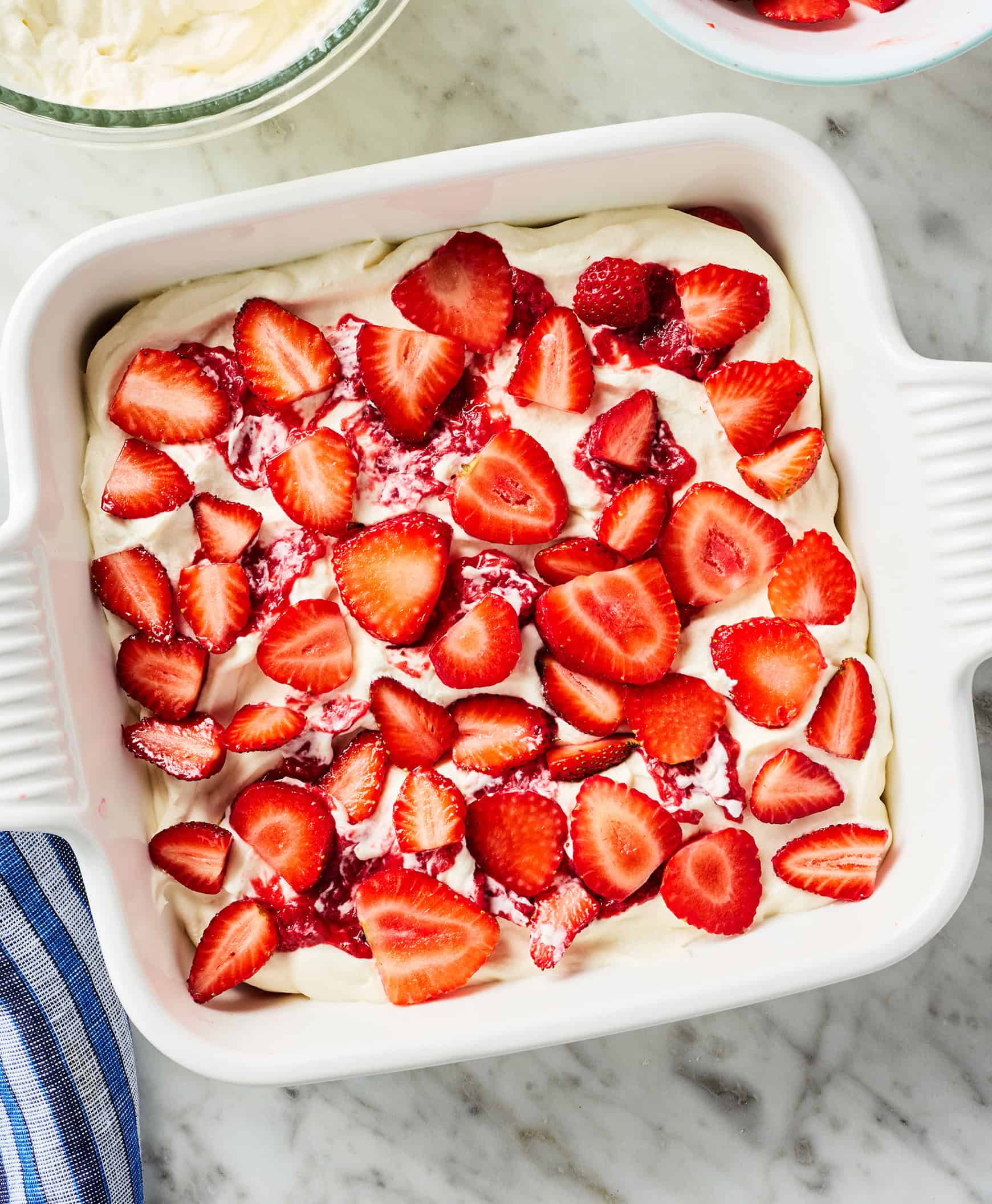 Cooked and fresh strawberries on top of cream mixture in baking dish