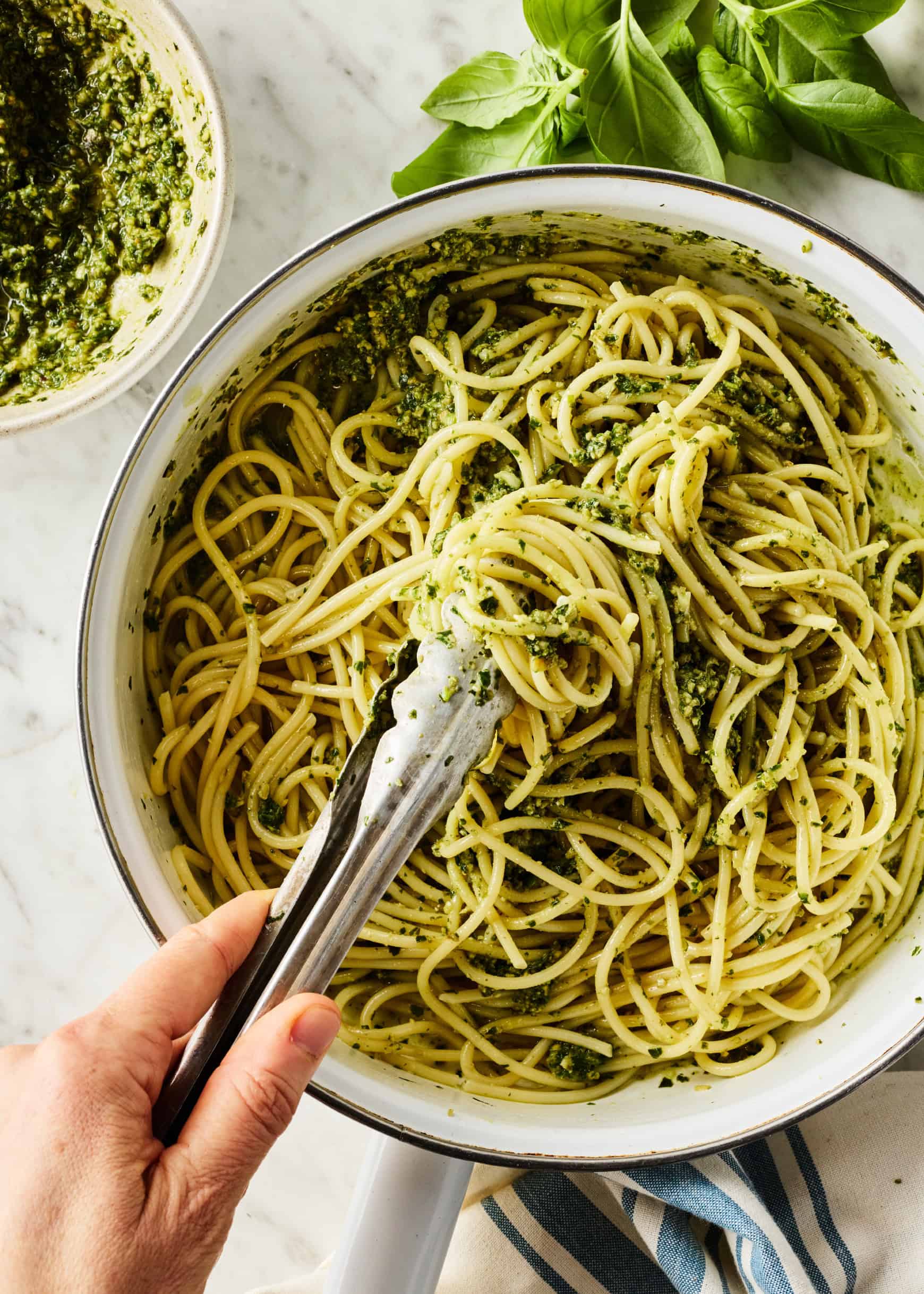 Tossing spaghetti with pesto sauce in skillet