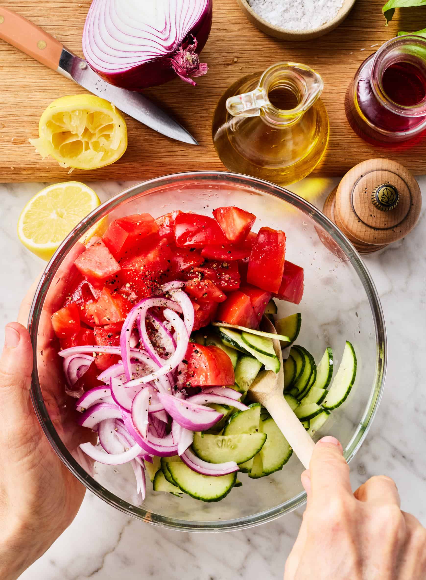 Tossing cucumbers, tomatoes, and onions in glass bowl
