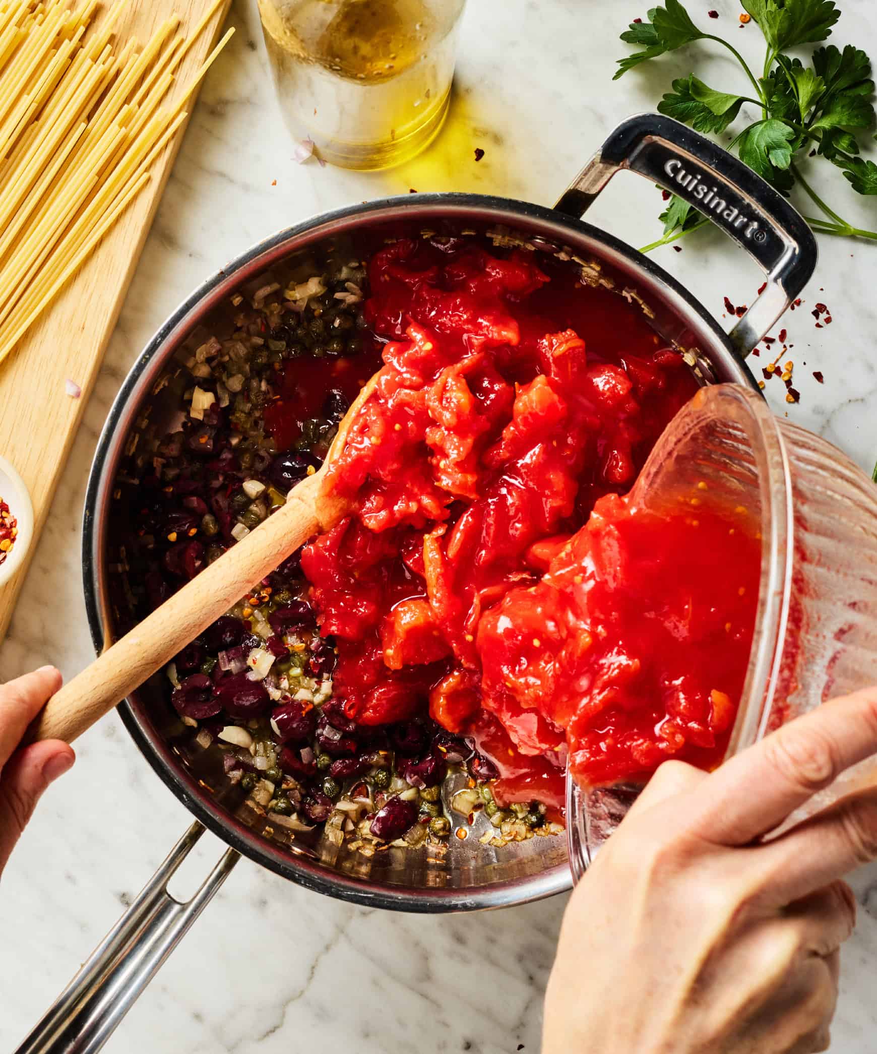 Adding canned tomatoes to skillet with capers and olives
