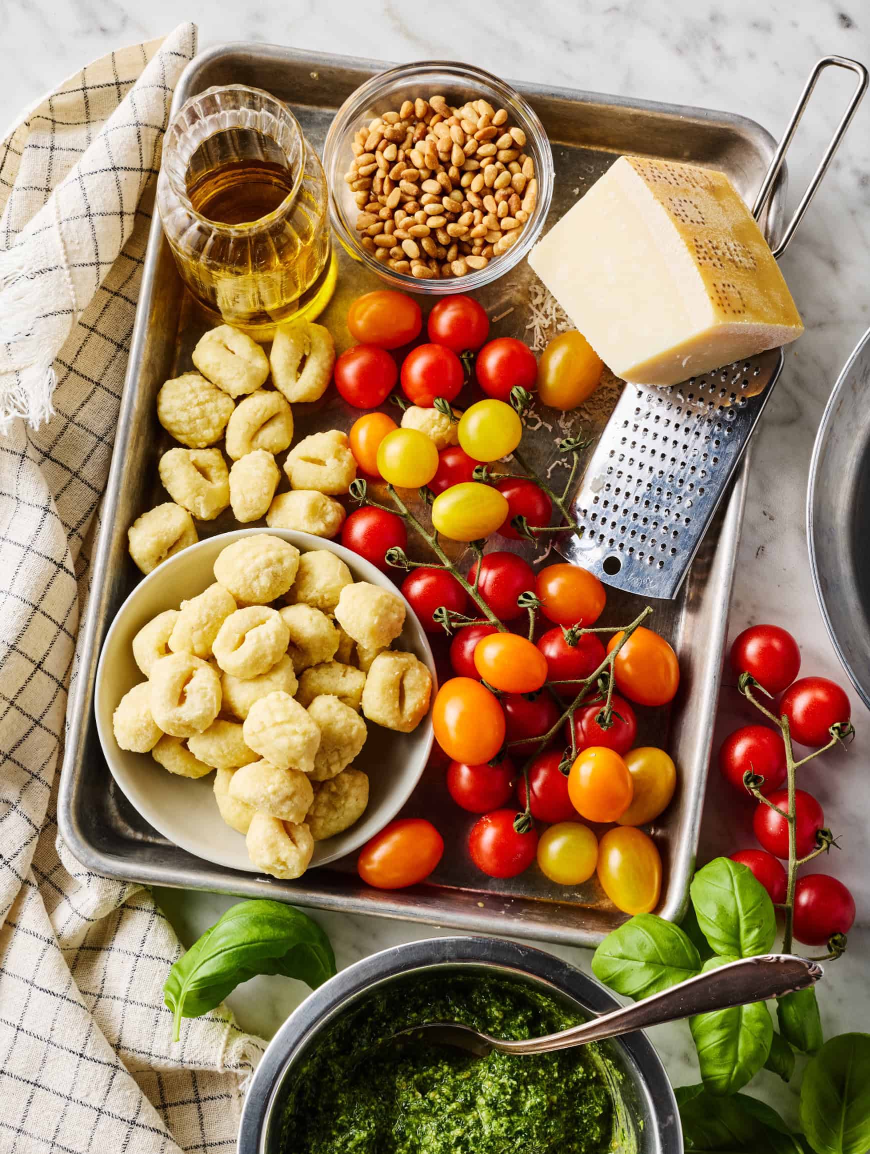 Gnocchi, cherry tomatoes, pine nuts, olive oil, and Parmesan on tray next to bowl of pesto