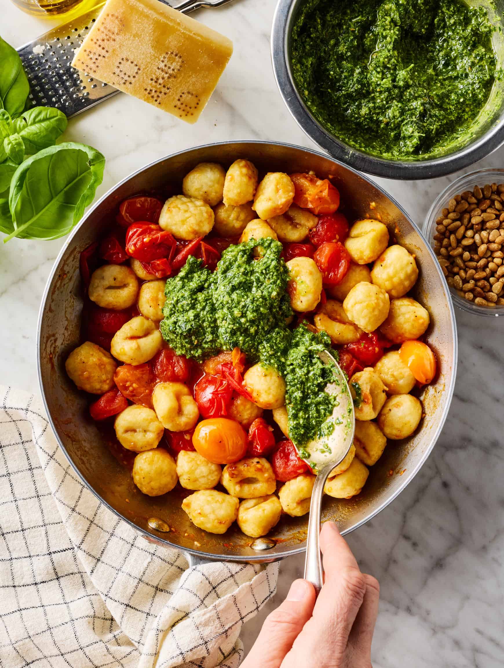 Spooning pesto over gnocchi and tomatoes in skillet