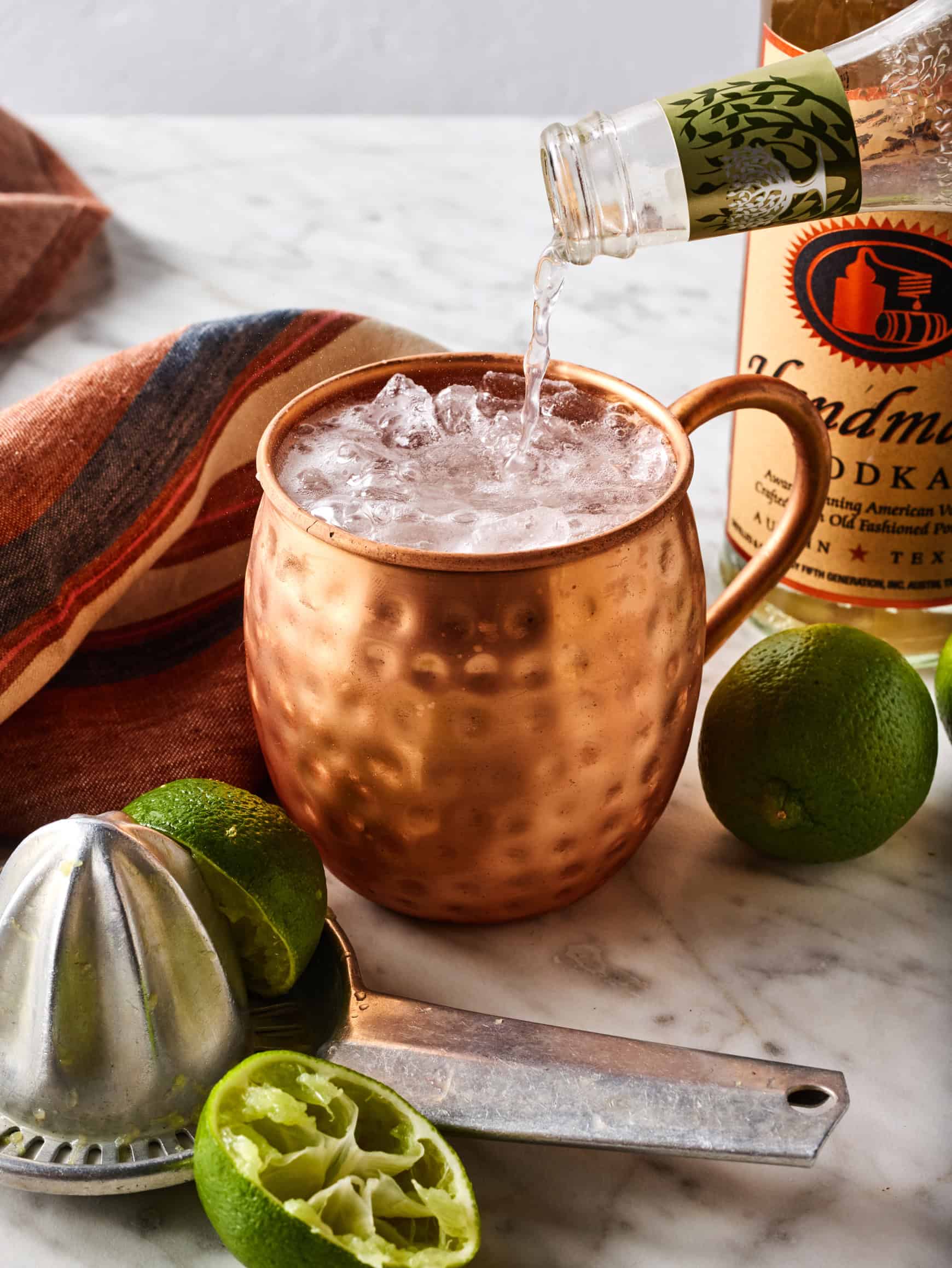 Pouring ginger beer into copper mugs with vodka, lime juice, and ice