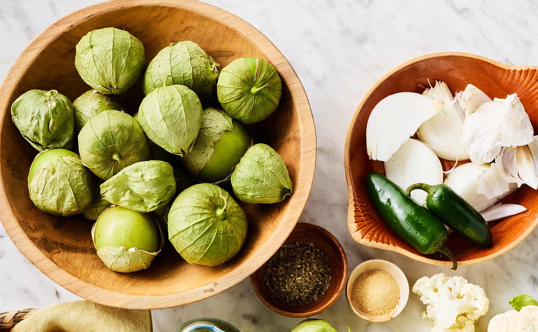 Bowl of tomatillos next to bowl of jalapeños and onion