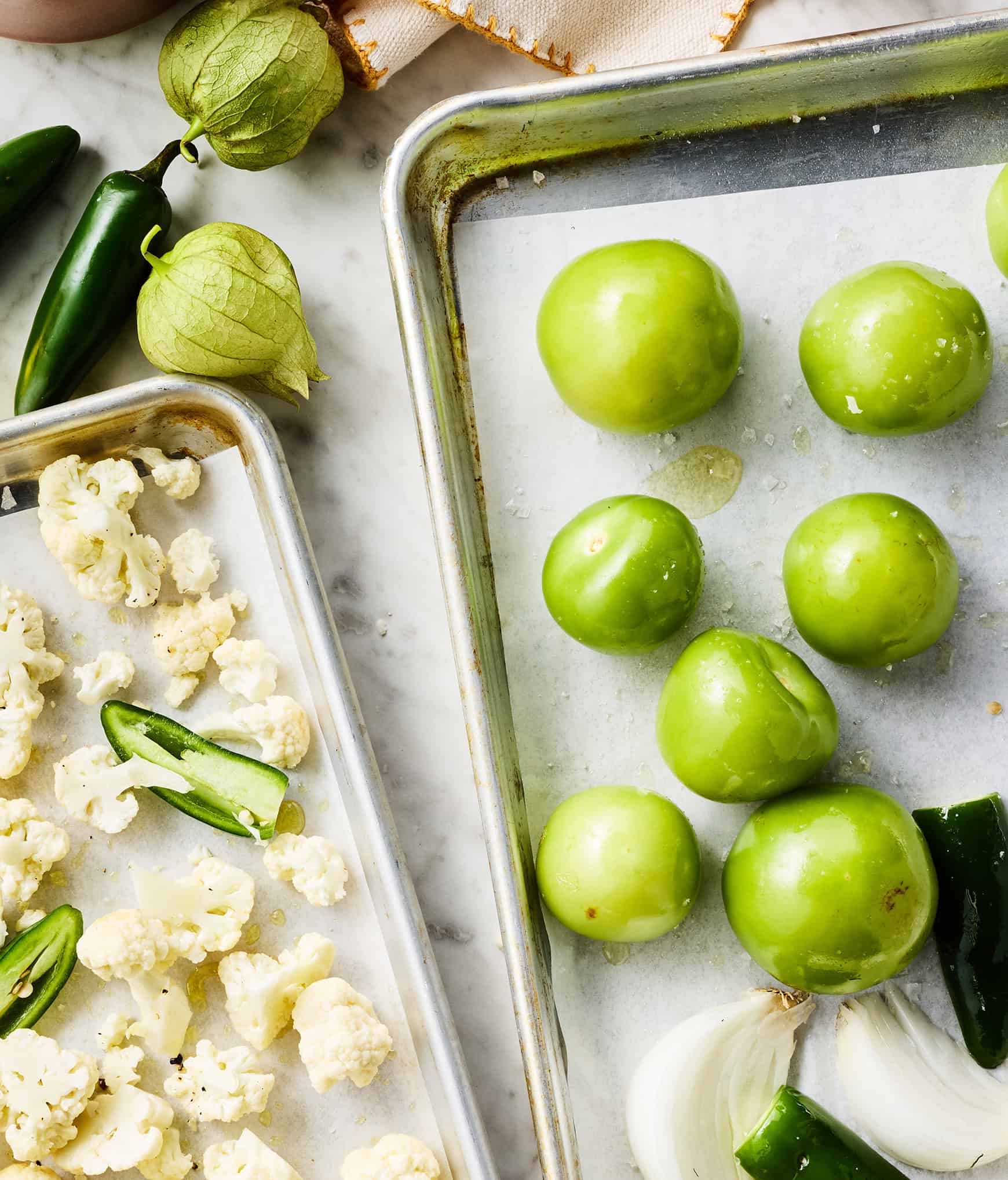 Tomatillos, onion, and jalapeños on baking sheets