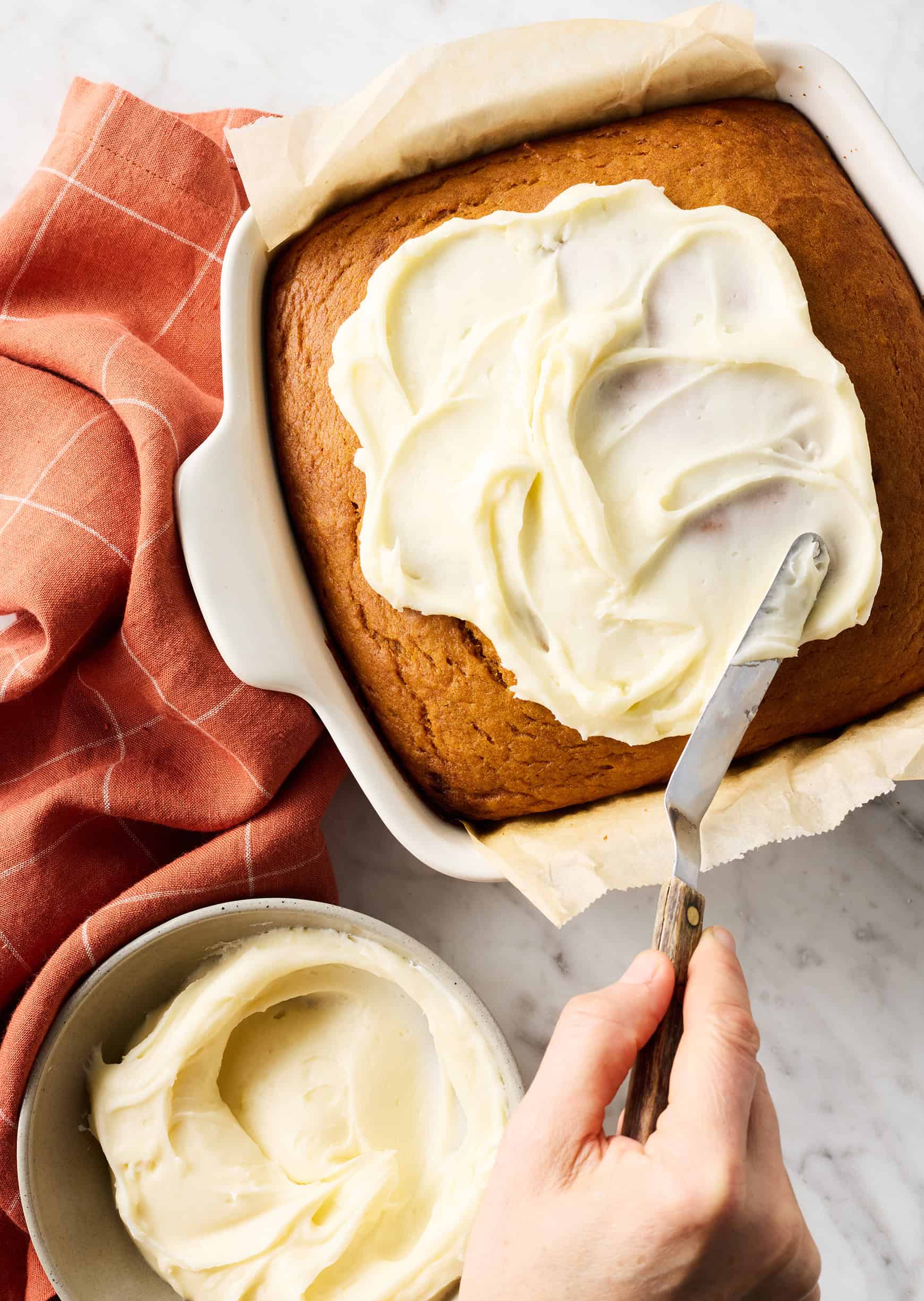 Spreading cream cheese frosting on pumpkin cake