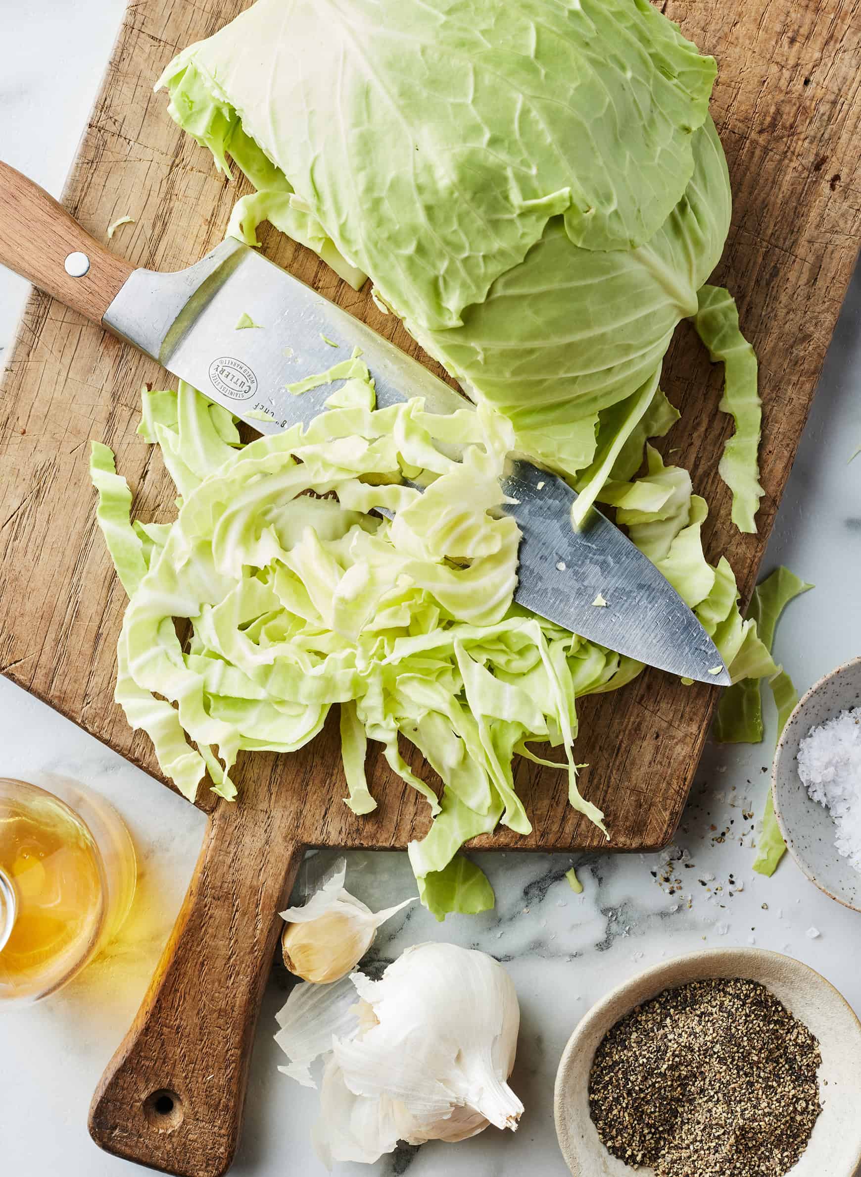 Thinly sliced green cabbage on cutting board with knife