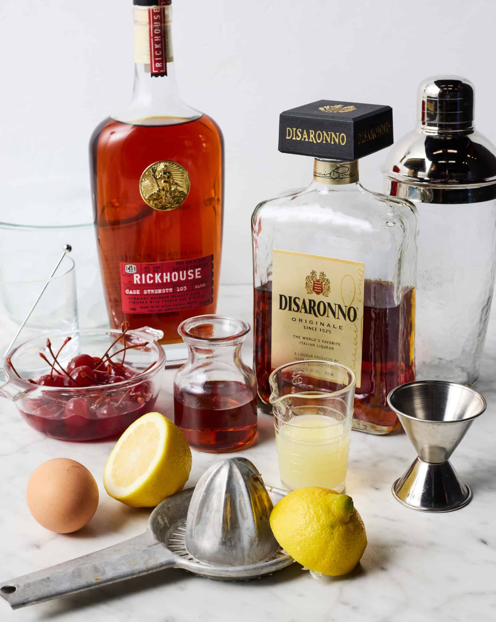 Amaretto sour ingredients - bourbon, amaretto, lemon juice, egg, and maraschino cherries