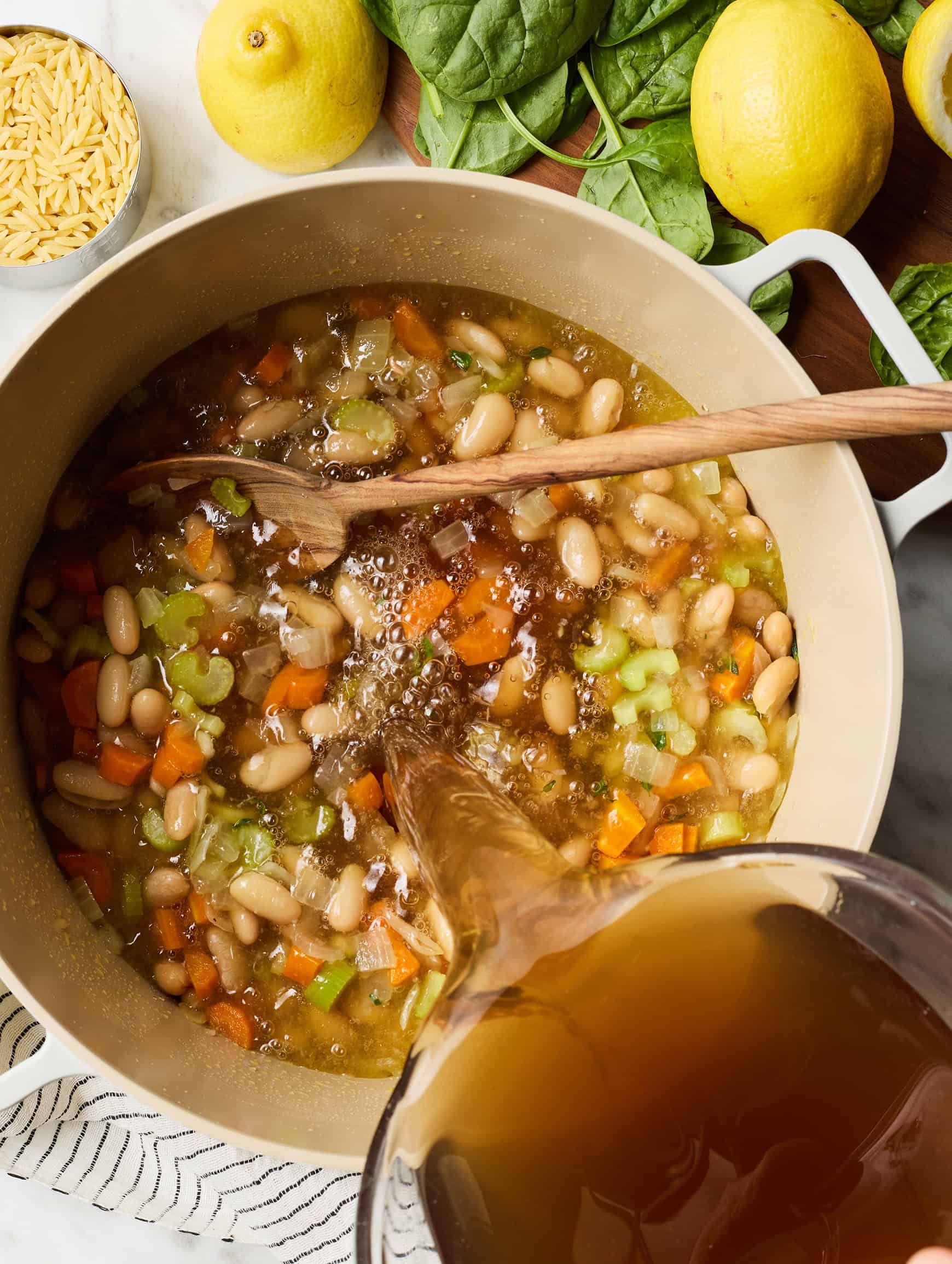 Pouring broth into soup pot with veggies and beans