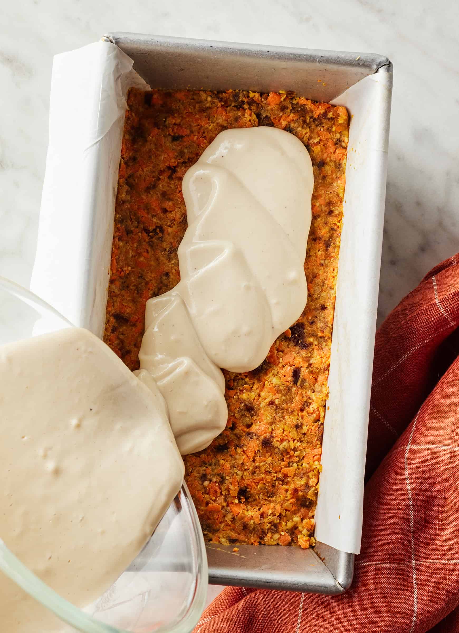 Pouring cashew frosting over carrot layer in loaf pan