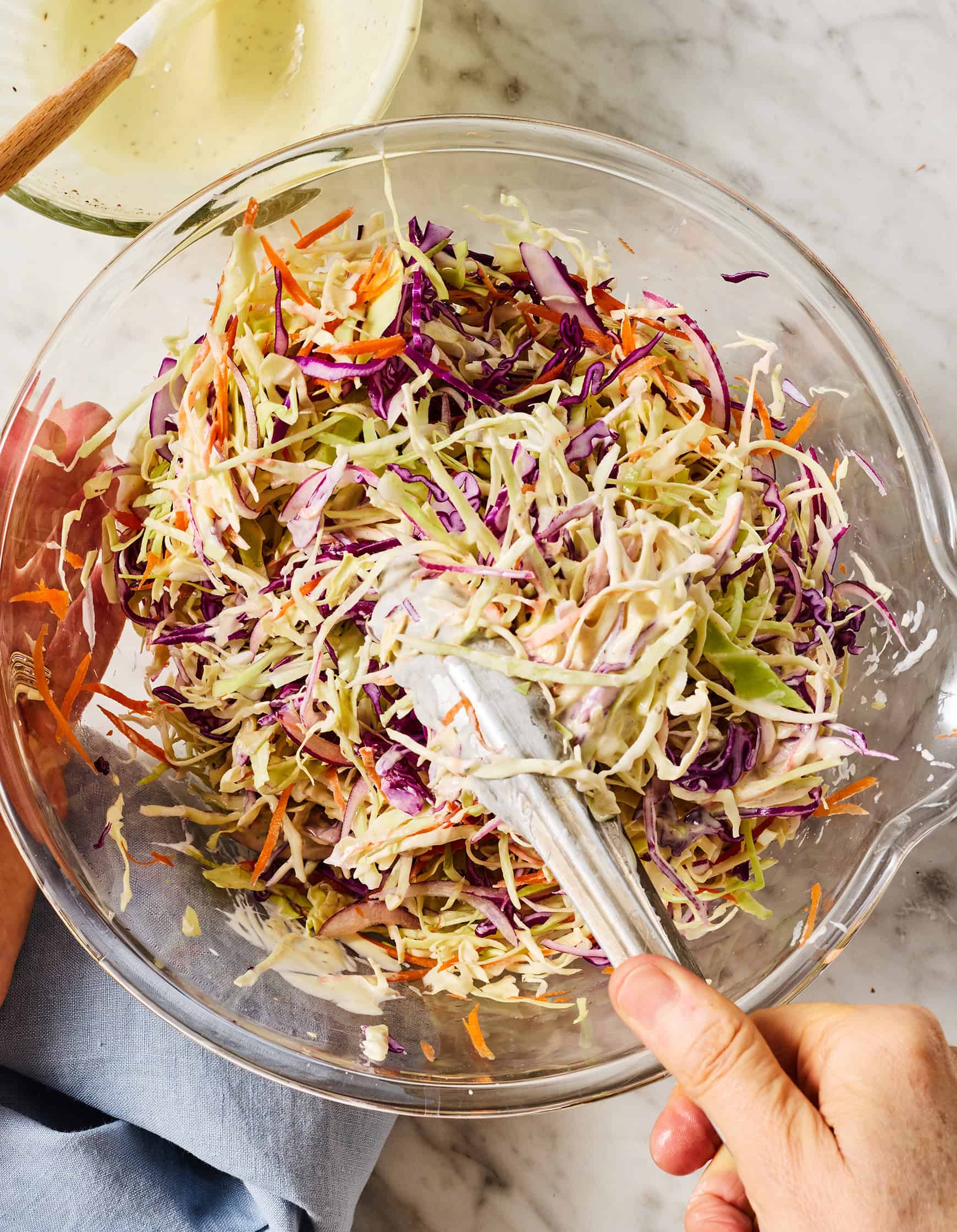 Mixing homemade coleslaw with tongs in glass bowl