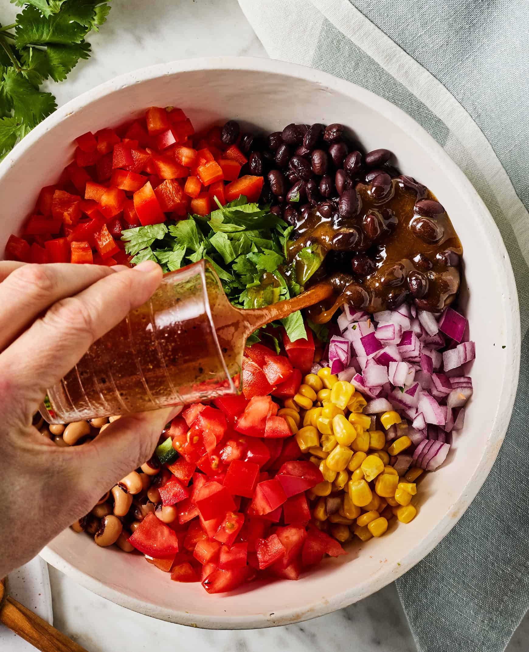 Pouring dressing over beans and vegetables in mixing bowl