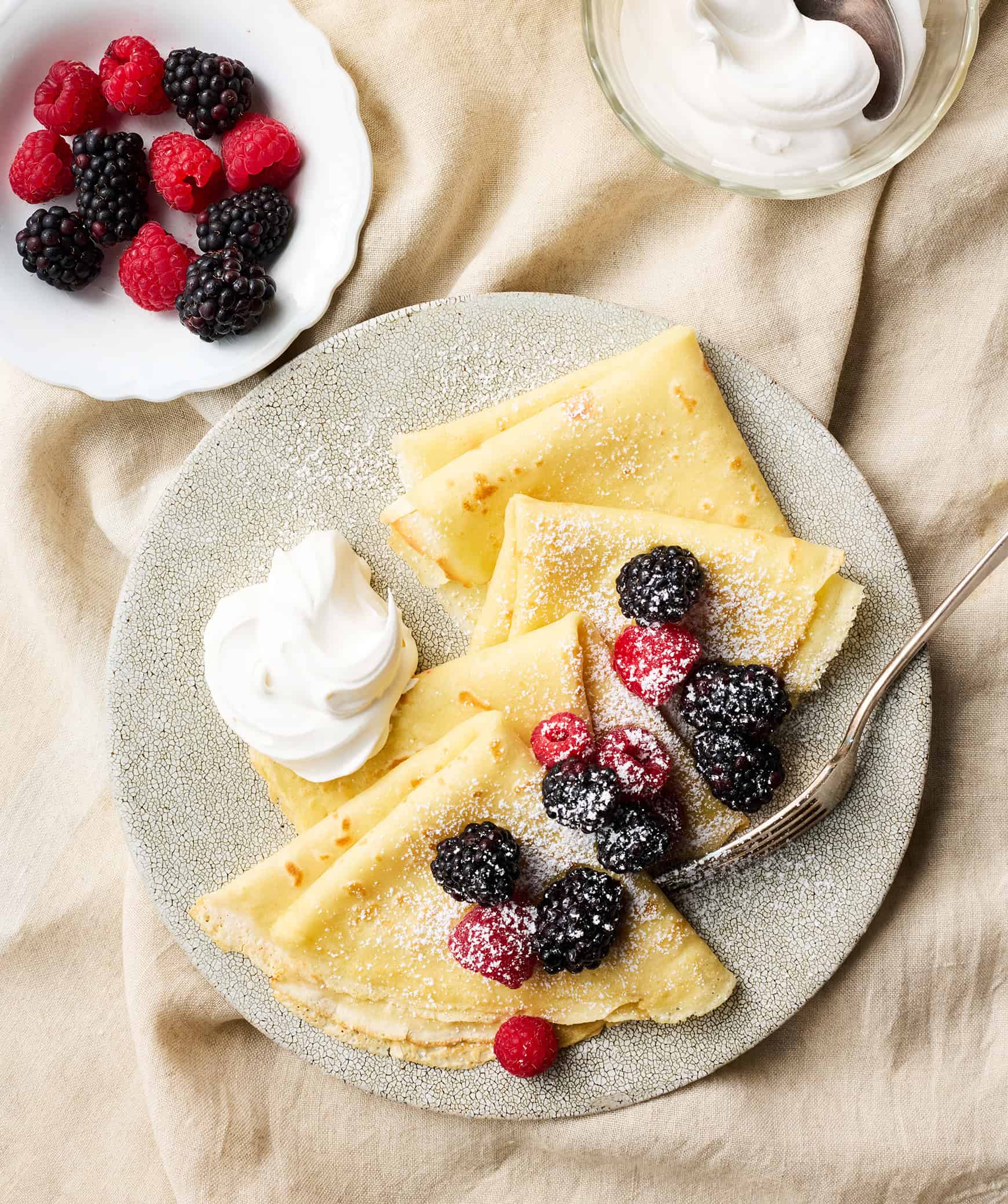 Crepes on plate with berries, cream, and powdered sugar