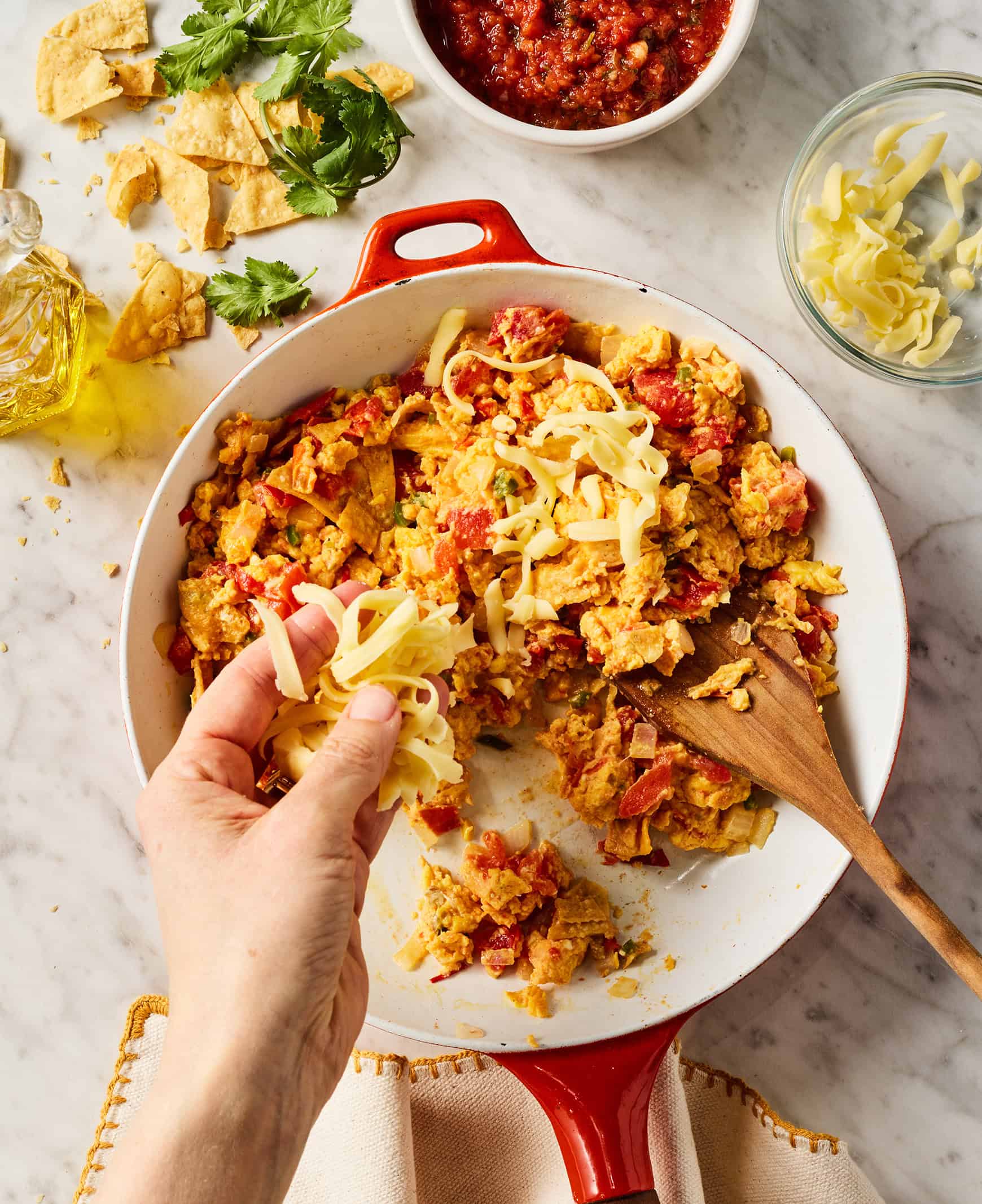 Adding cheese to skillet with eggs, tortilla chips, and veggies
