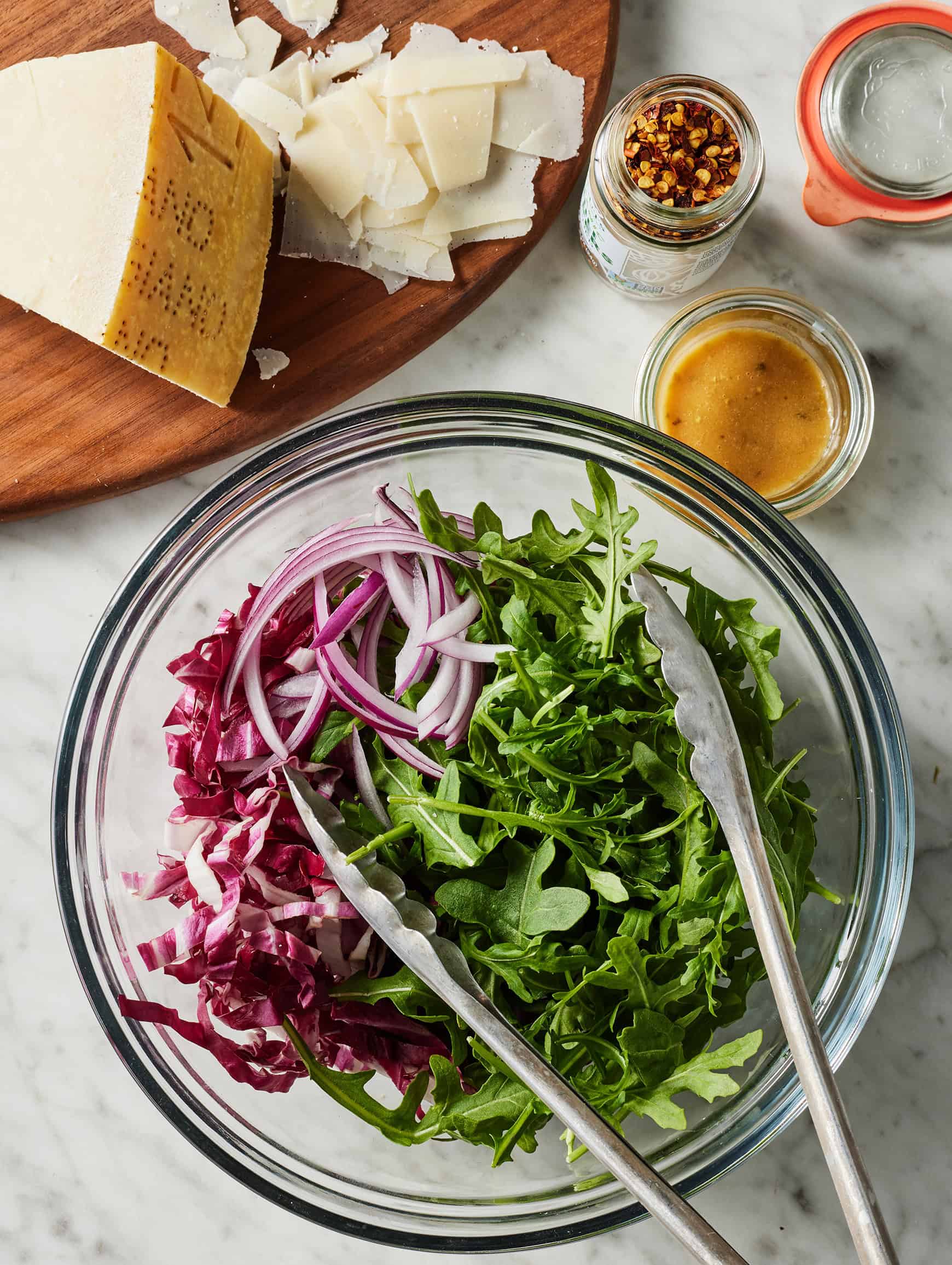 Arugula, radicchio, and red onion in glass mixing bowl with tongs