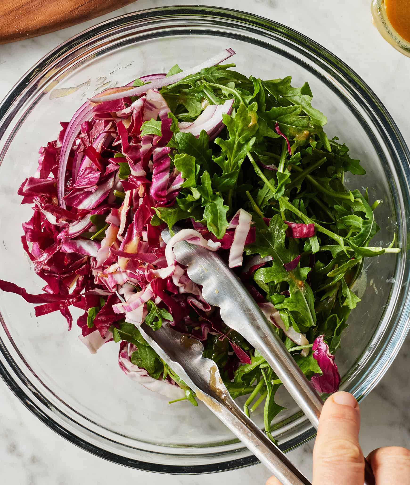 Tossing salad with red wine vinaigrette in glass bowl