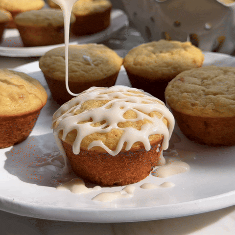 Spooning lemon glaze over zesty ricotta muffins on white plate