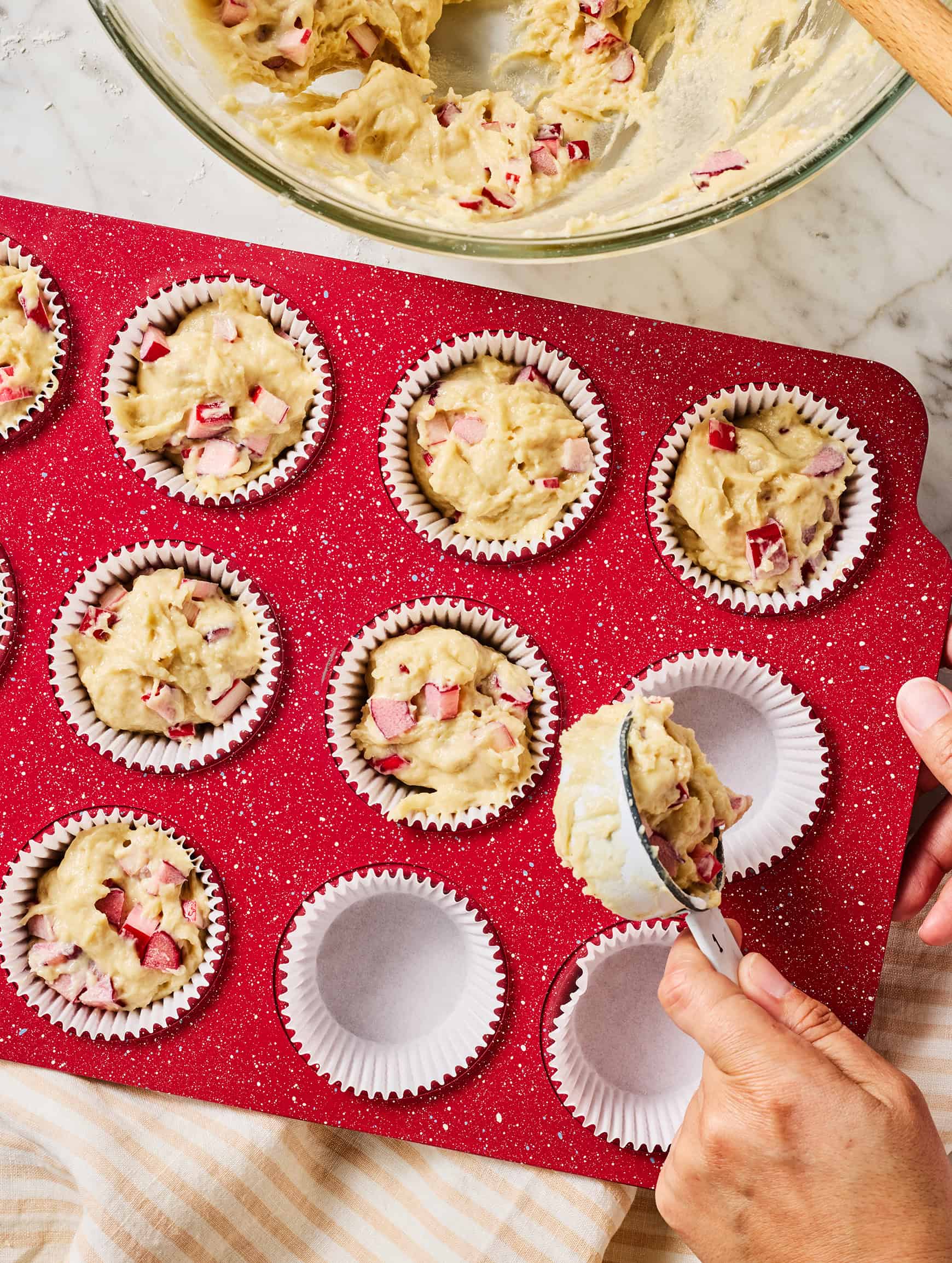 Scooping batter for rhubarb muffins into muffin tin with liners