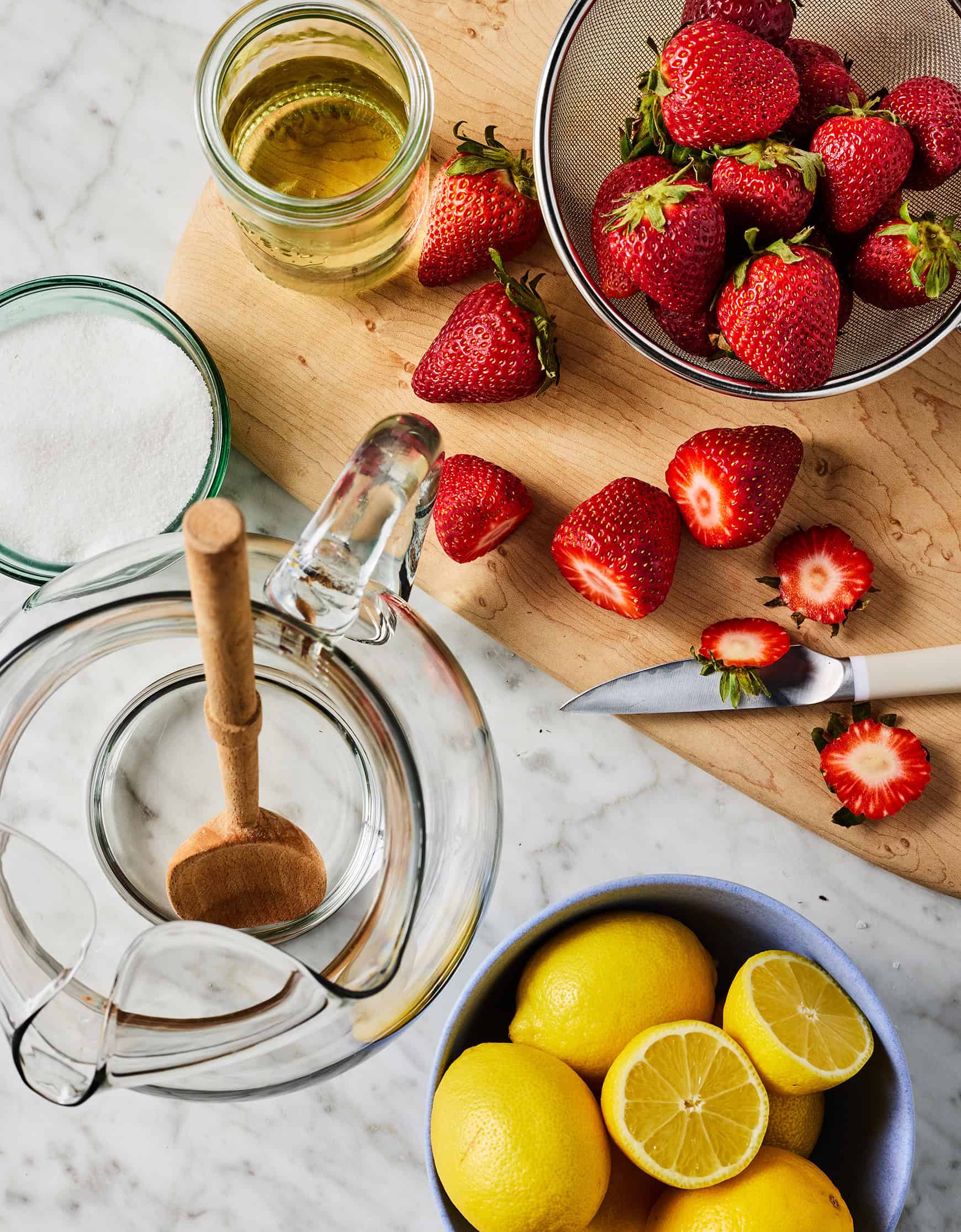 Recipe ingredients (fresh strawberries, lemons, sugar, and simple syrup) on countertop