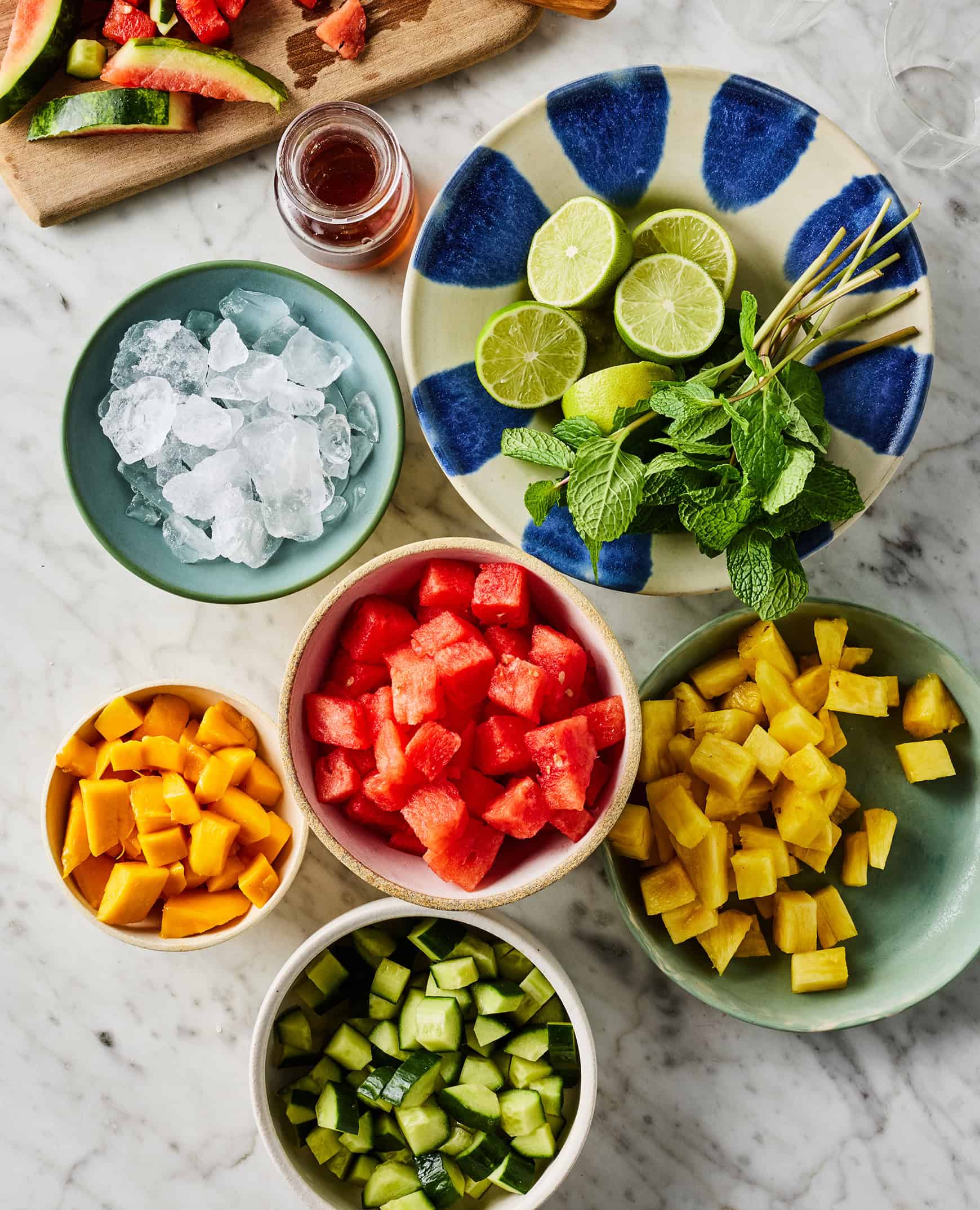 Recipe ingredients - fresh pineapple, mango, watermelon, cucumber, mint, lime, and agave - on marble countertop