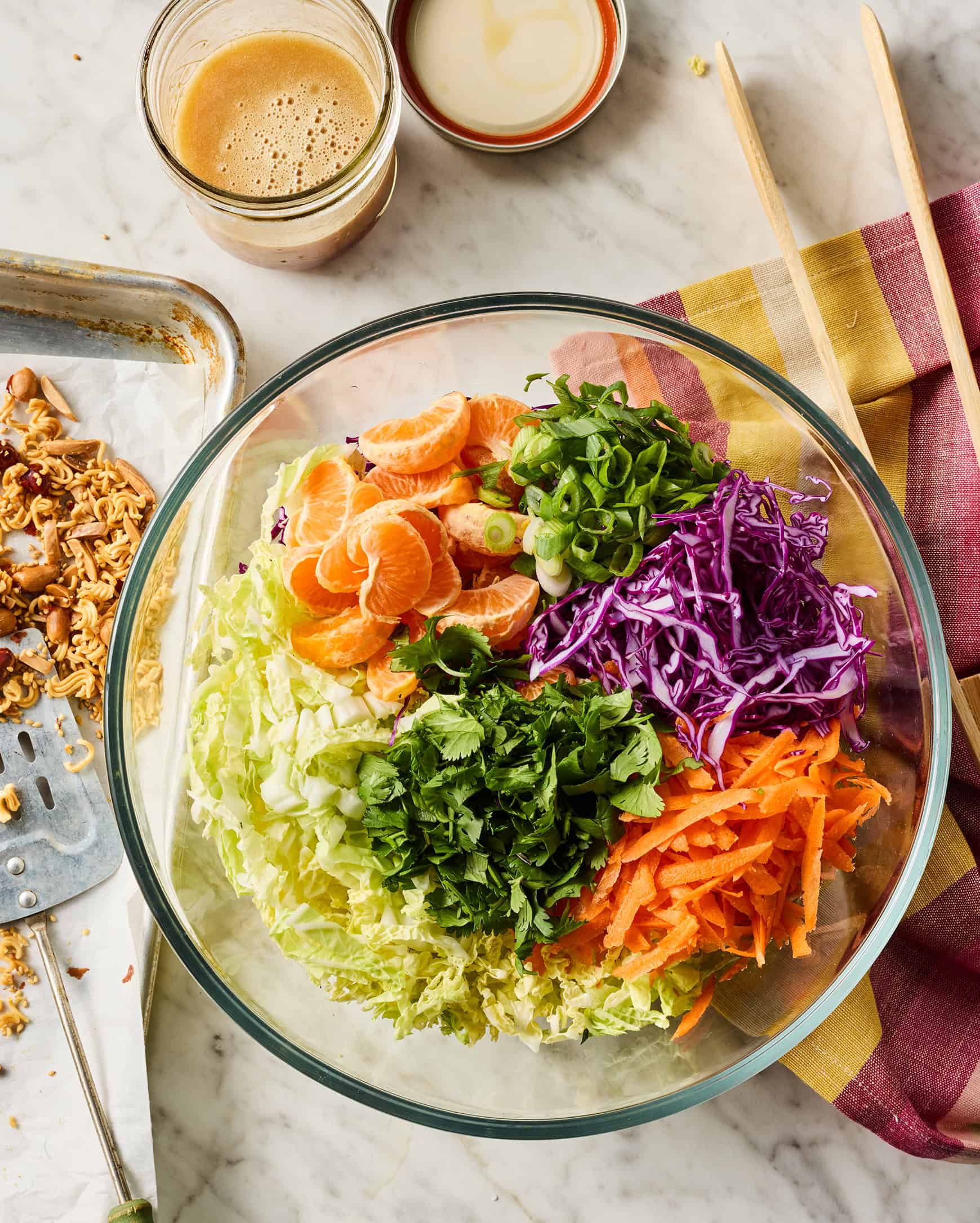 Shredded cabbage, carrots, scallions, cilantro, and mandarin oranges segmented in glass mixing bowl