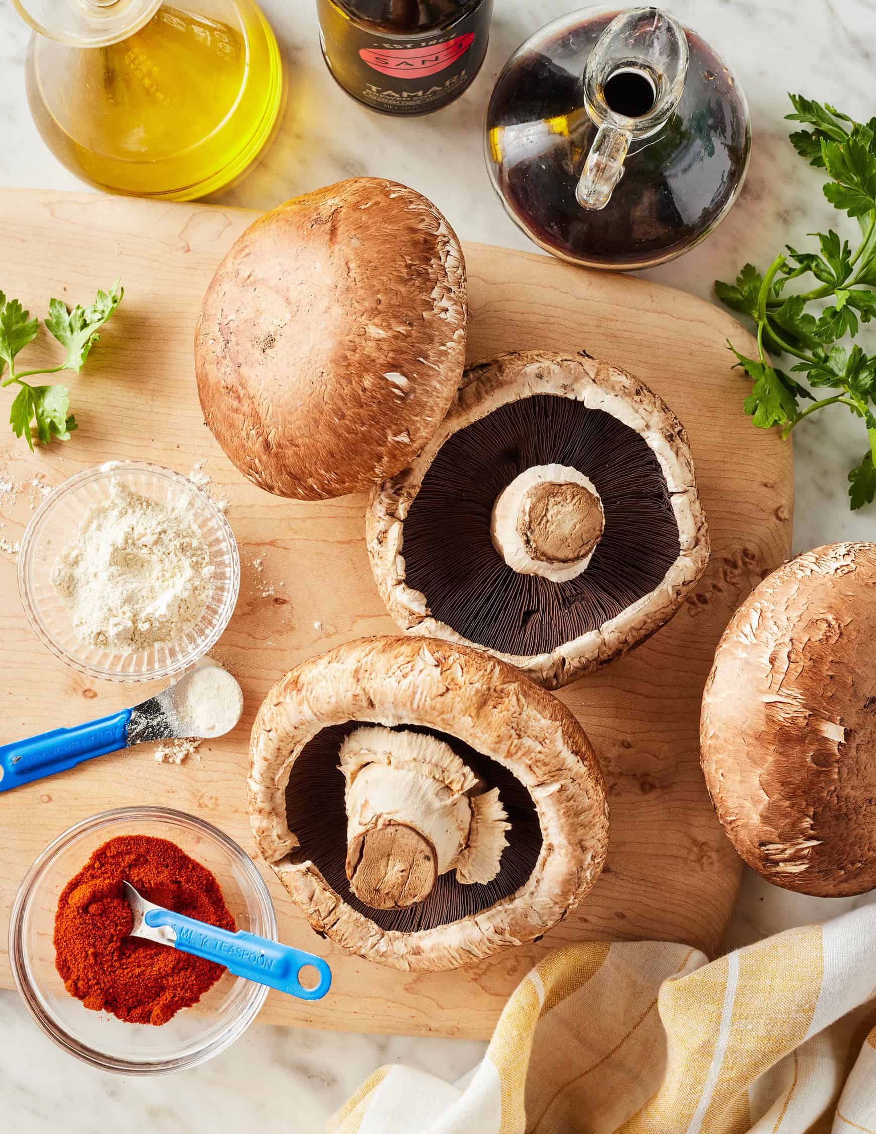 Portobello mushrooms on cutting board next to spices, balsamic vinegar, tamari, and olive oil