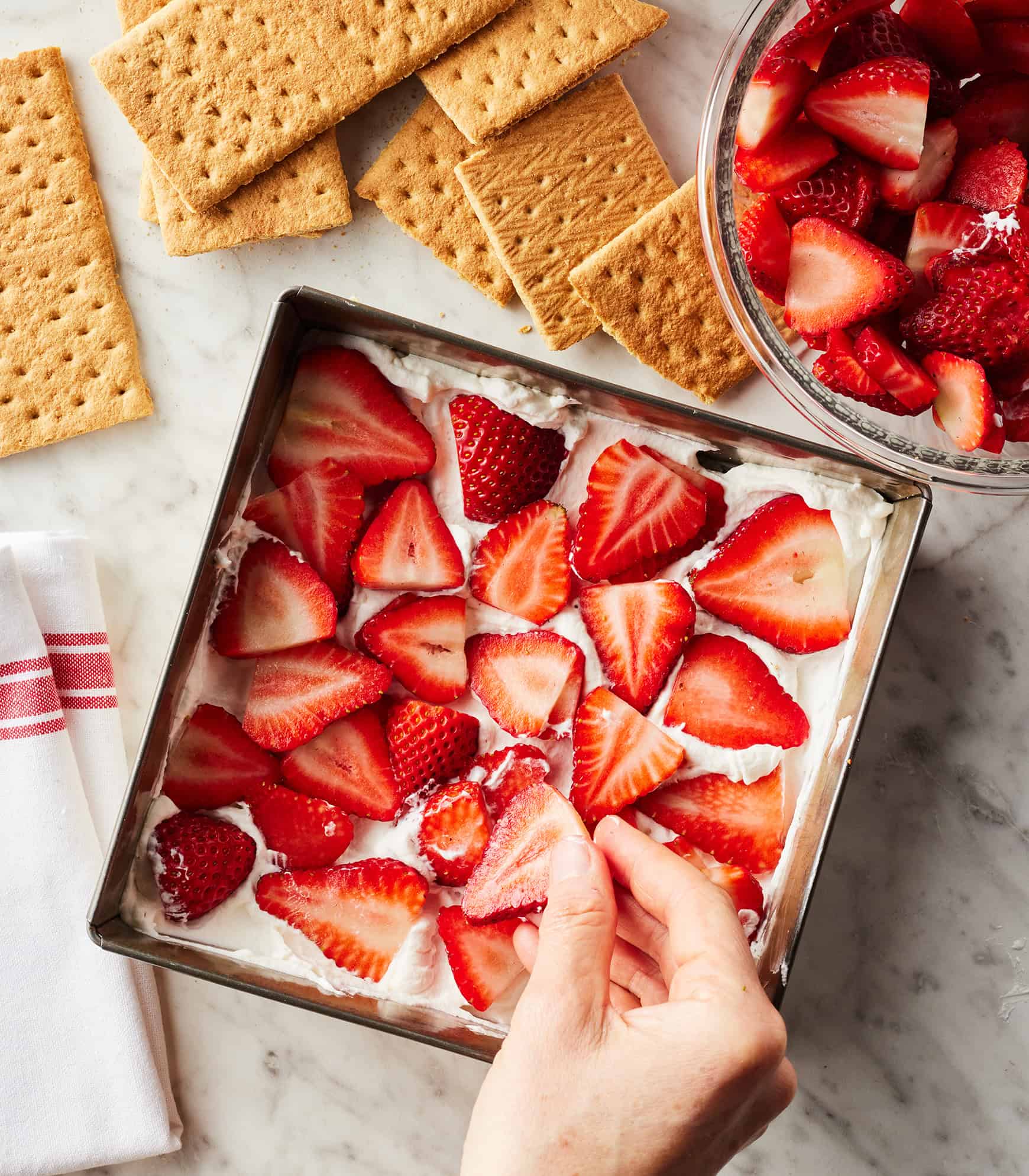 Layering strawberries onto whipped cream in square baking dish