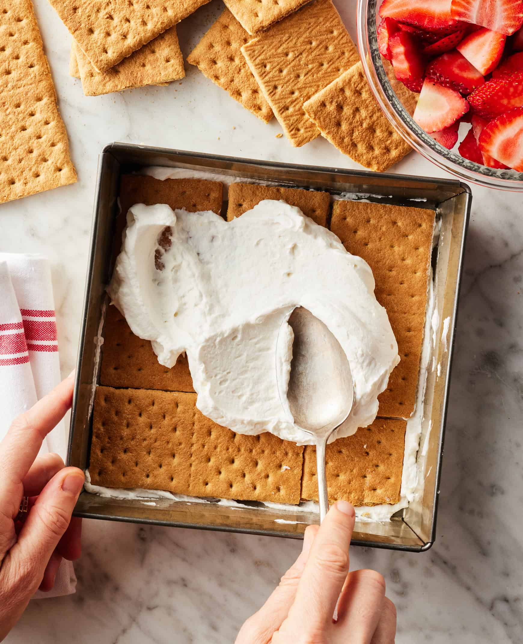 Spreading layer of whipped cream over graham crackers in square baking dish