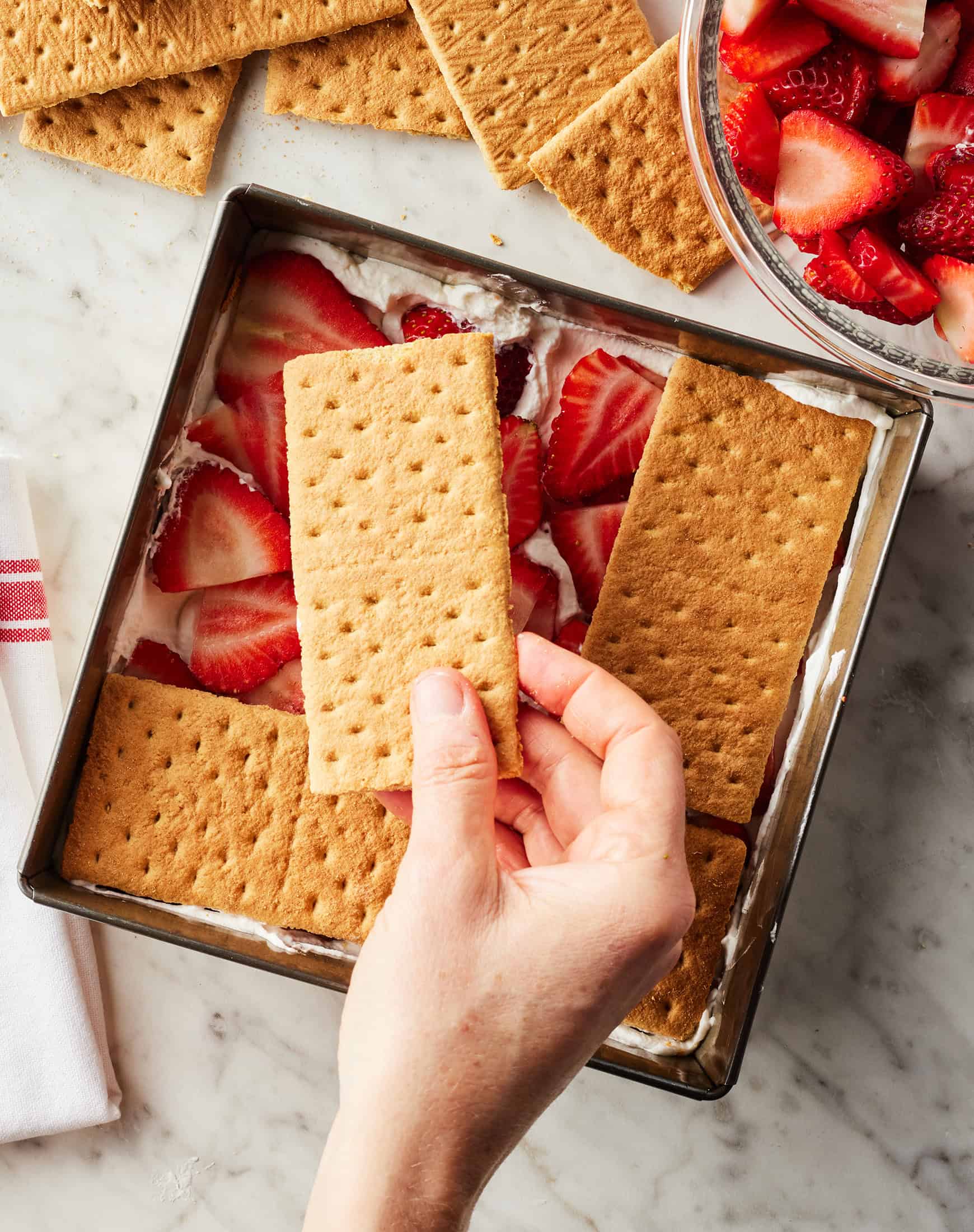 Assembling strawberry icebox cake by adding a second layer of graham crackers on top of berries in baking dish