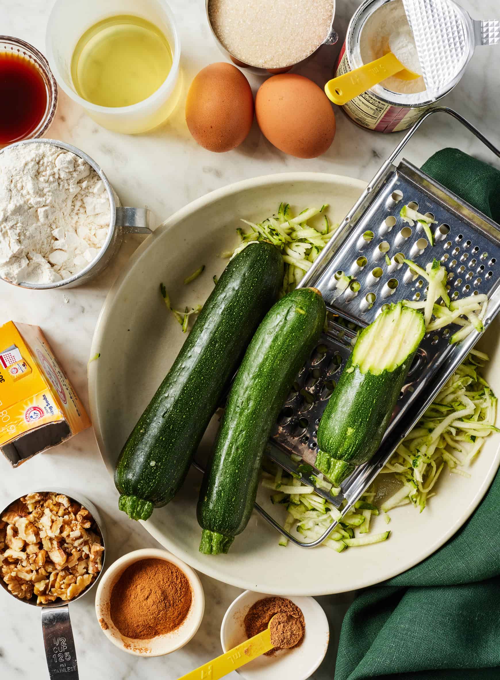 Recipe ingredients - shredded zucchini, eggs, flour, sugar, spices, and walnuts on countertop