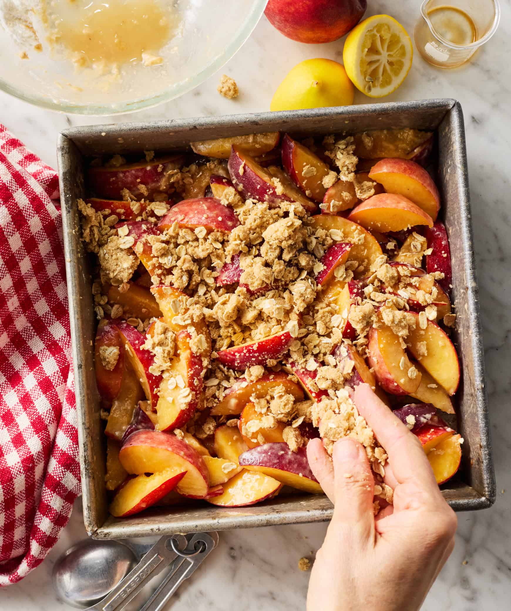 Sprinkling crumble topping over peaches in baking dish