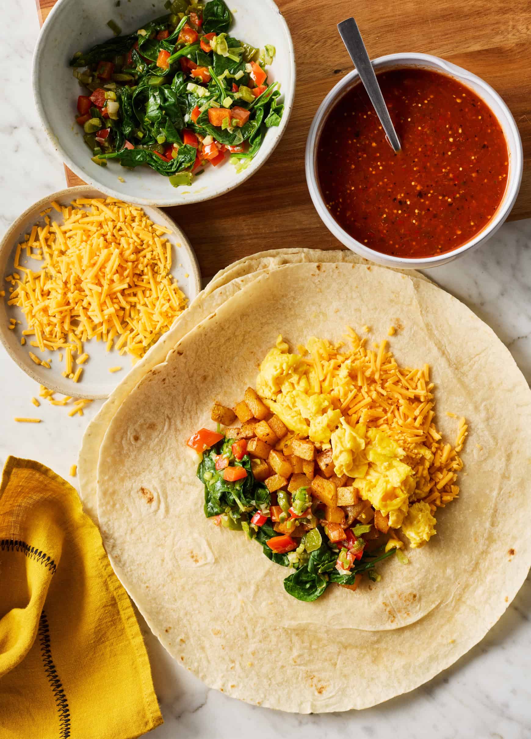 Cheese, scrambled eggs, roasted potatoes, and veggies in center of large flour tortilla