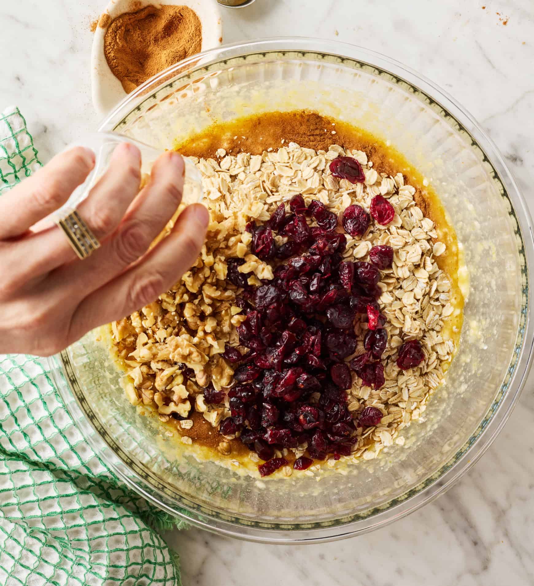 Adding walnuts, cranberries, and oats to bowl with wet ingredients