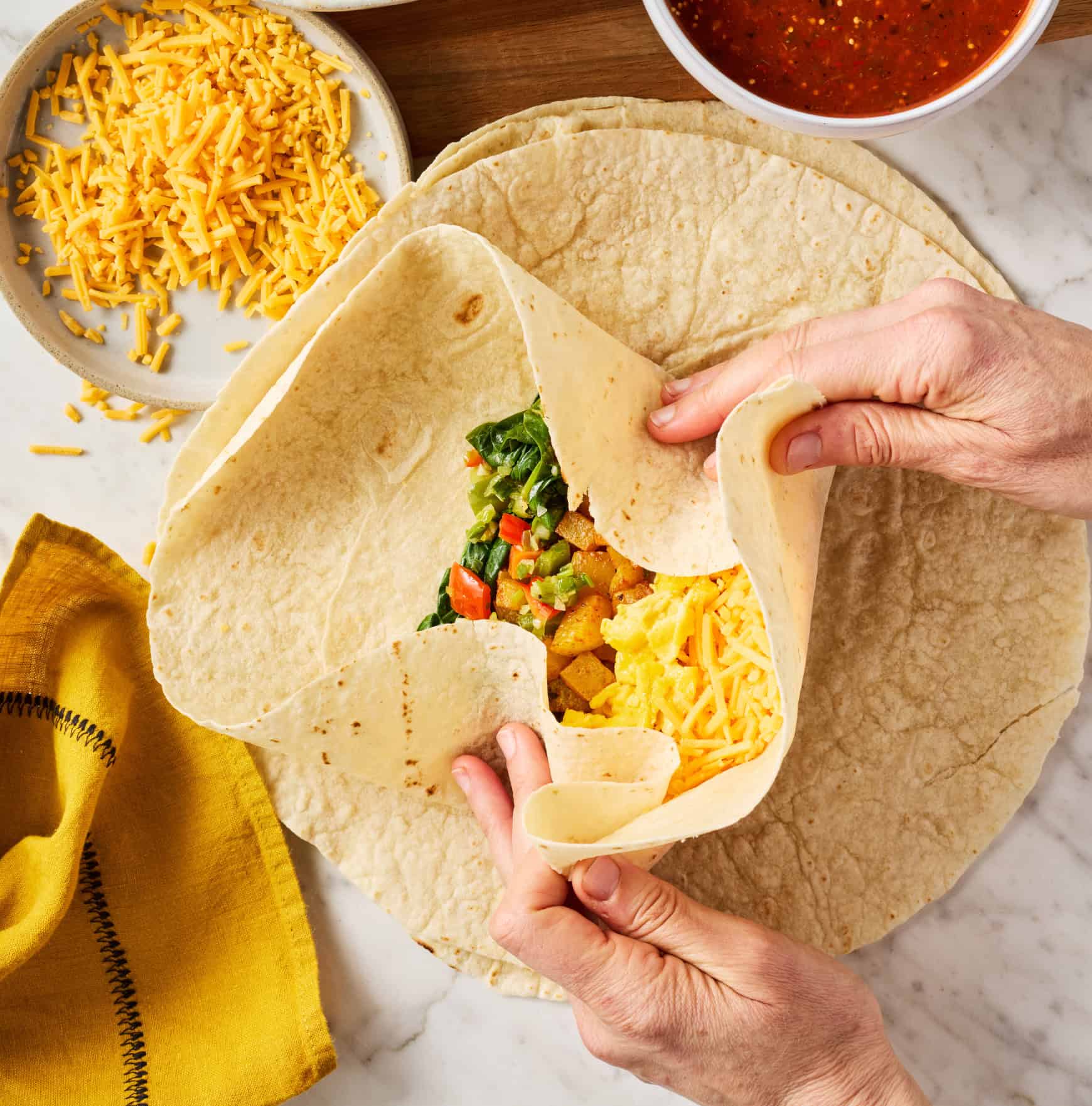 Hands rolling breakfast burrito closed