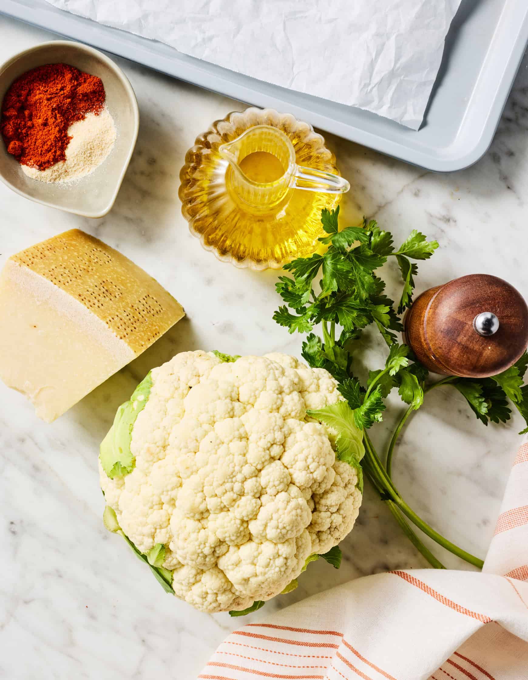 Recipe ingredients on countertop: cauliflower, olive oil, parsley, spices, and Parmesan cheese